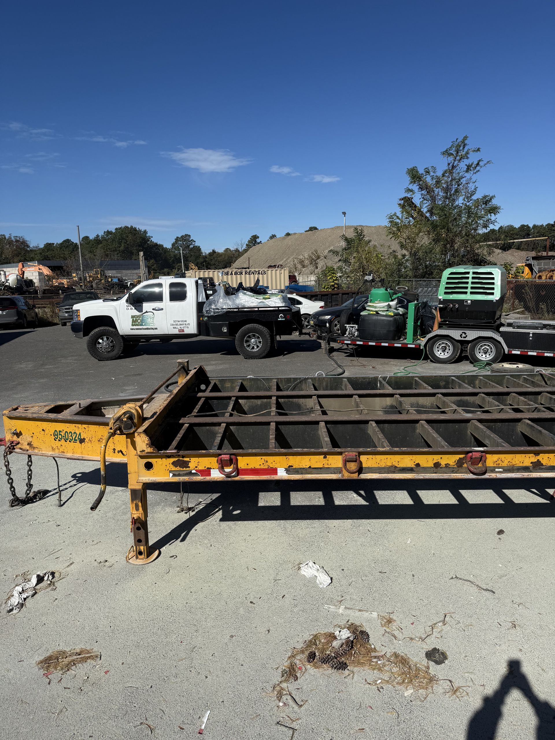 Truck pulling a trailer with a wood chipper; another empty trailer in foreground. Outdoors, sunny.