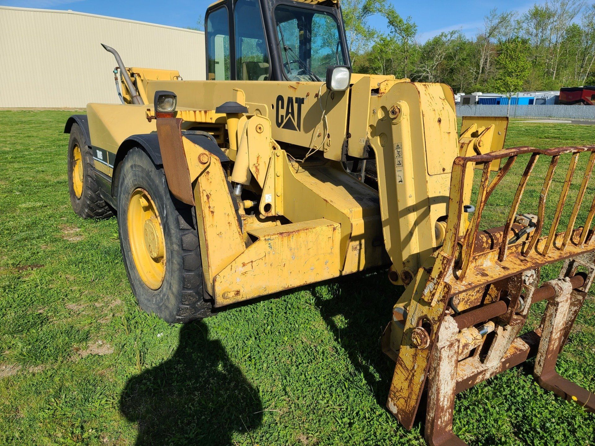 Yellow Caterpillar telehandler on a grassy field, showing its forks and a raised boom.