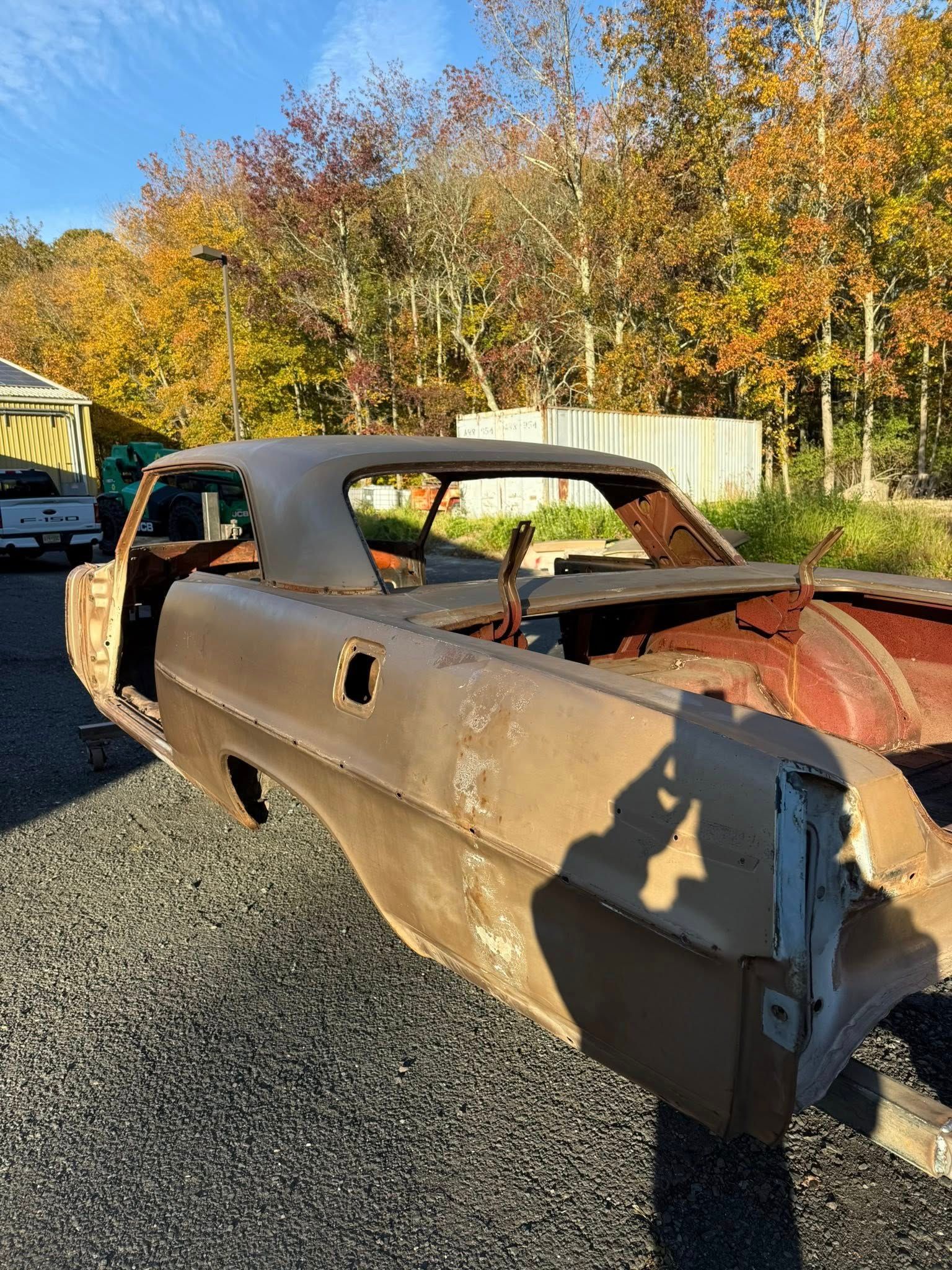 Rusting car body in a natural setting, missing parts.