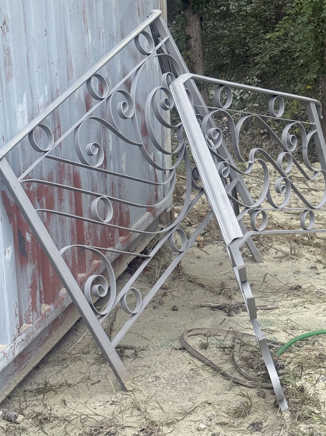 Two decorative metal fence panels, gray, leaning against a weathered metal structure outdoors.