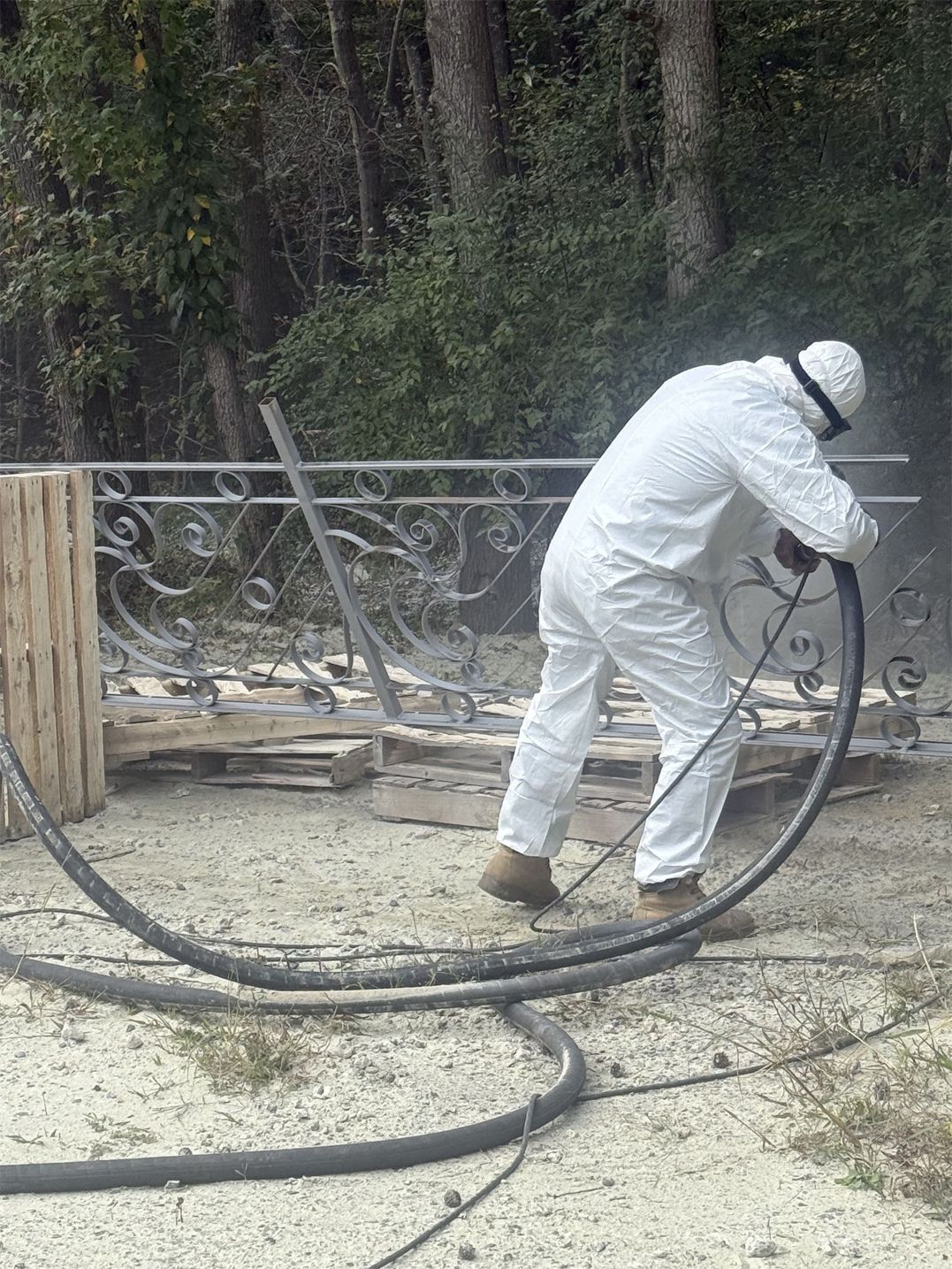 Person in protective suit sandblasting an ornate metal gate outdoors.