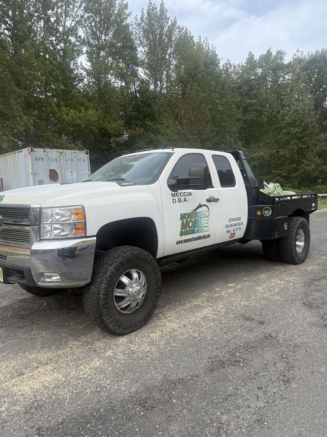 White Chevy dually pickup truck with flatbed, logo on side. Outdoors, daytime.