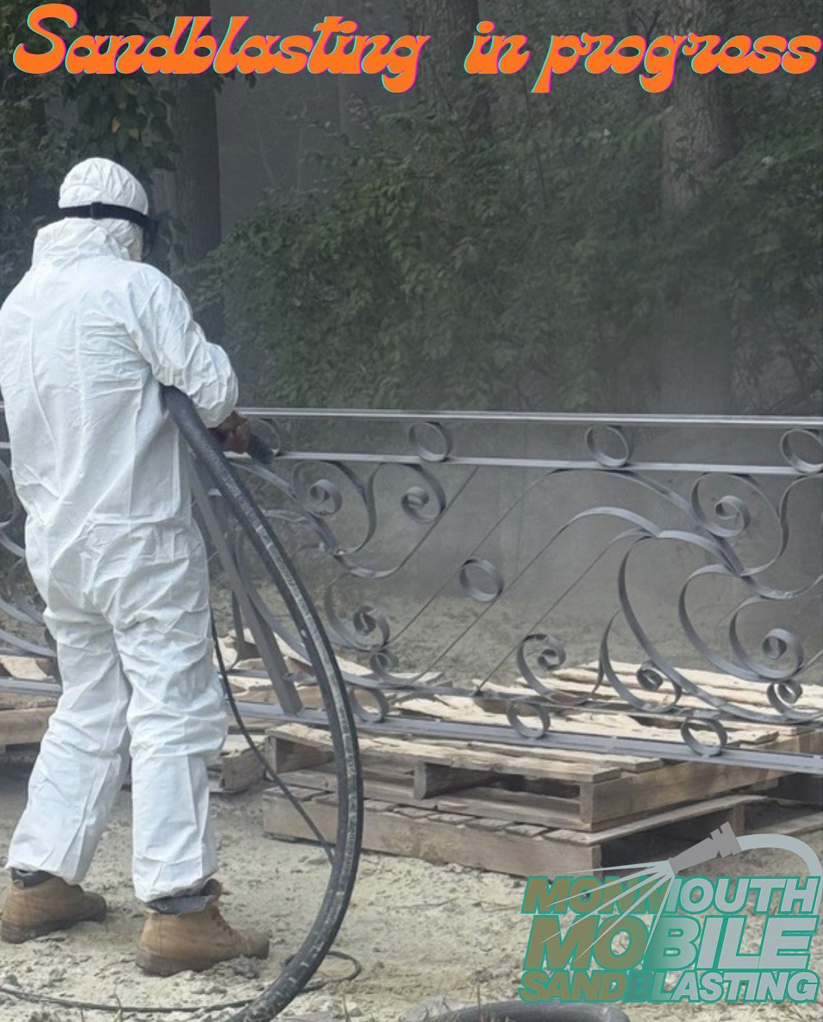 Person in white protective suit sandblasting a decorative metal railing outdoors.
