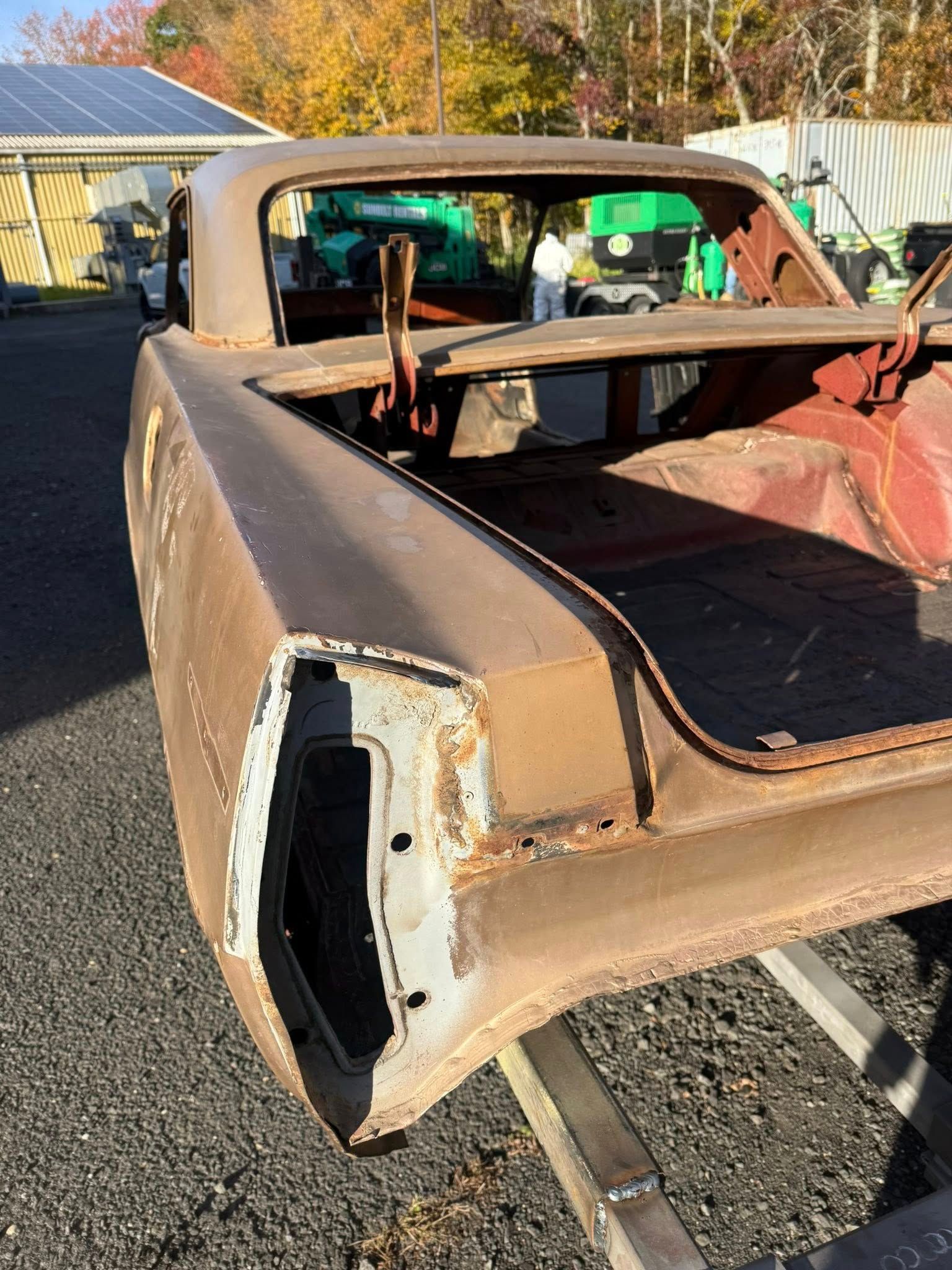 Rusty car body with open trunk and exposed rear. Outdoor, daytime.