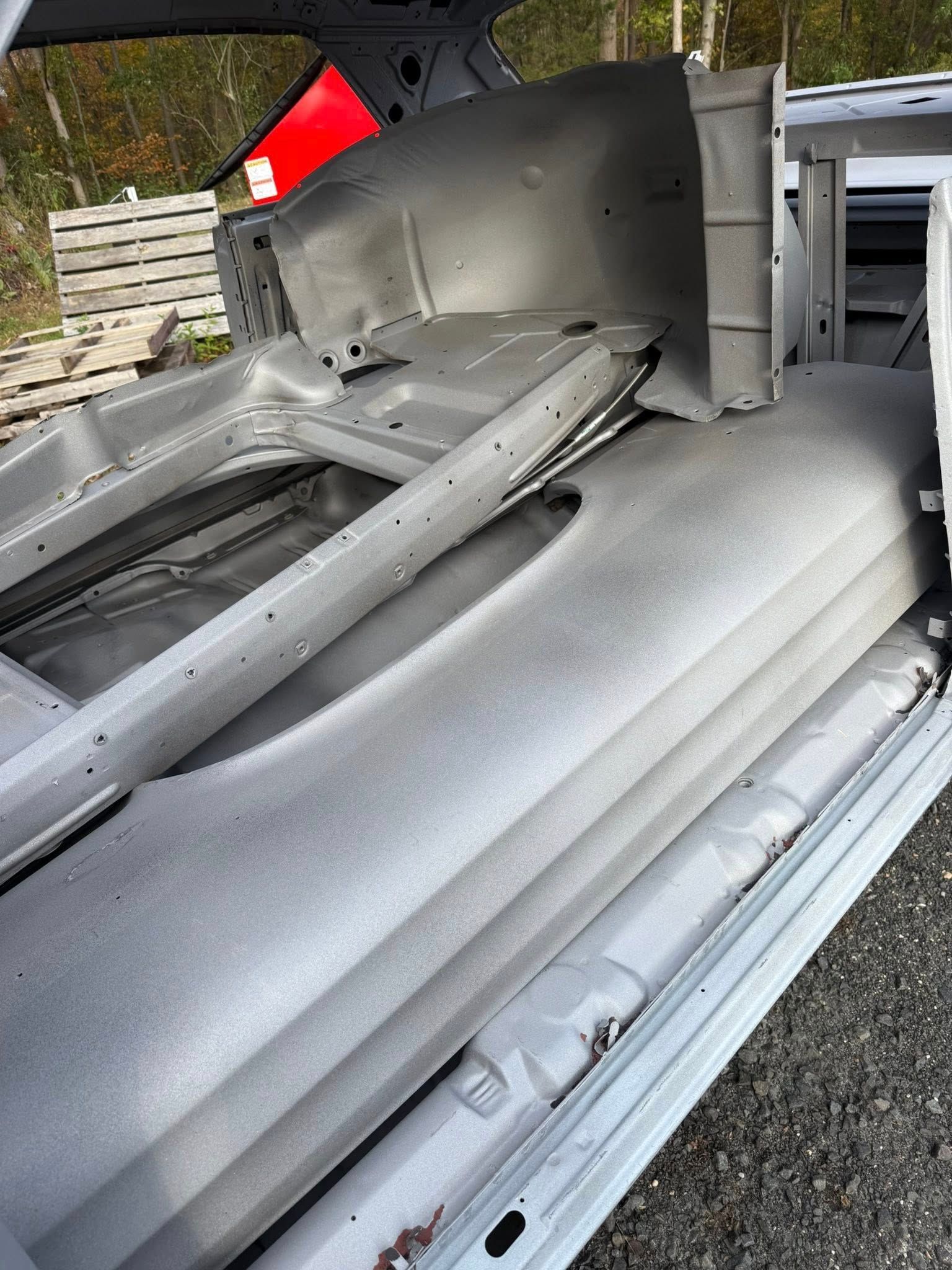Gray car body sections stacked outdoors, likely for restoration.