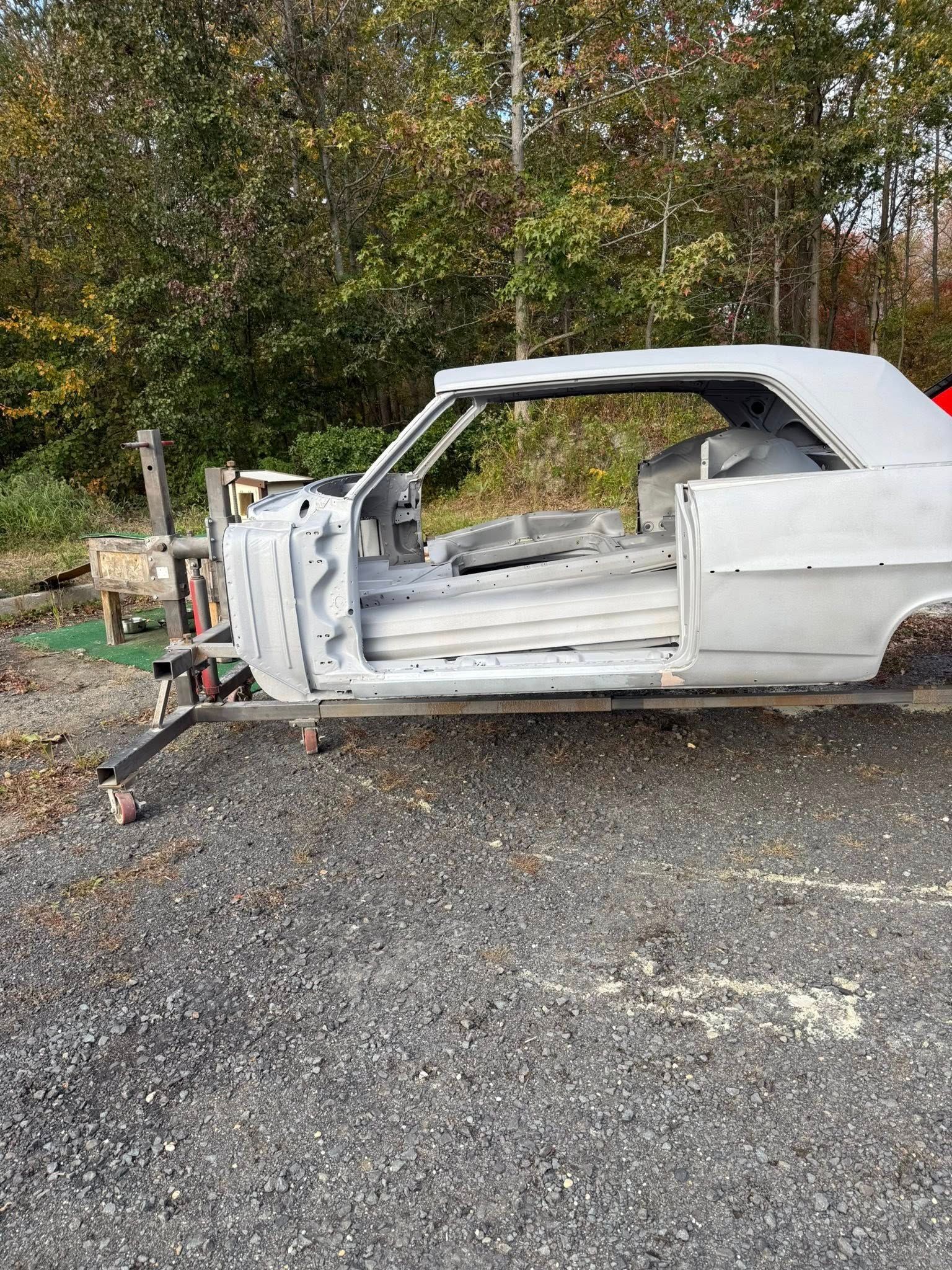 Bare-bones convertible car frame on a wheeled stand, outdoors, ready for restoration.