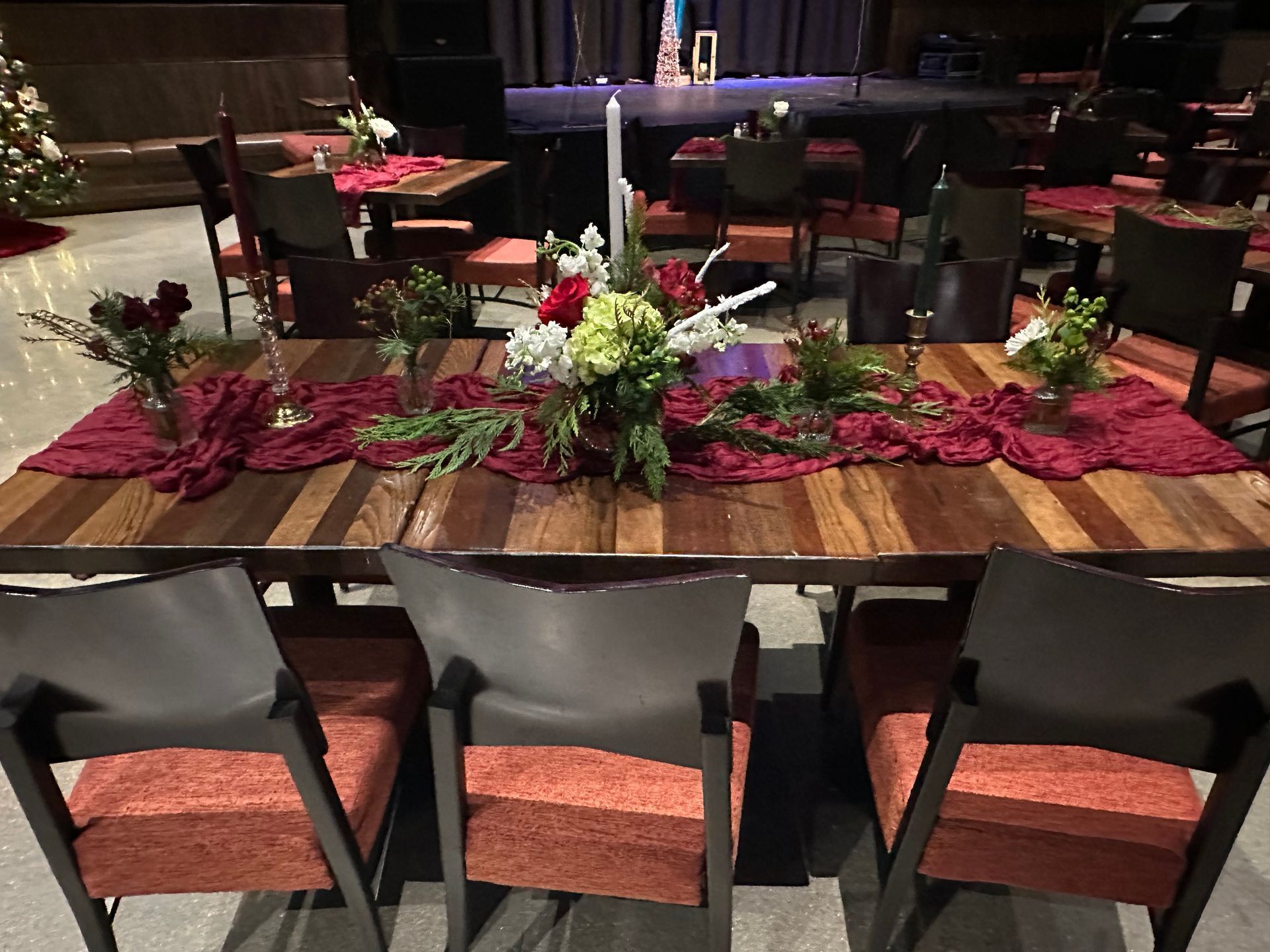Formal dining table set with maroon runner and floral centerpieces. Chairs are around the table.