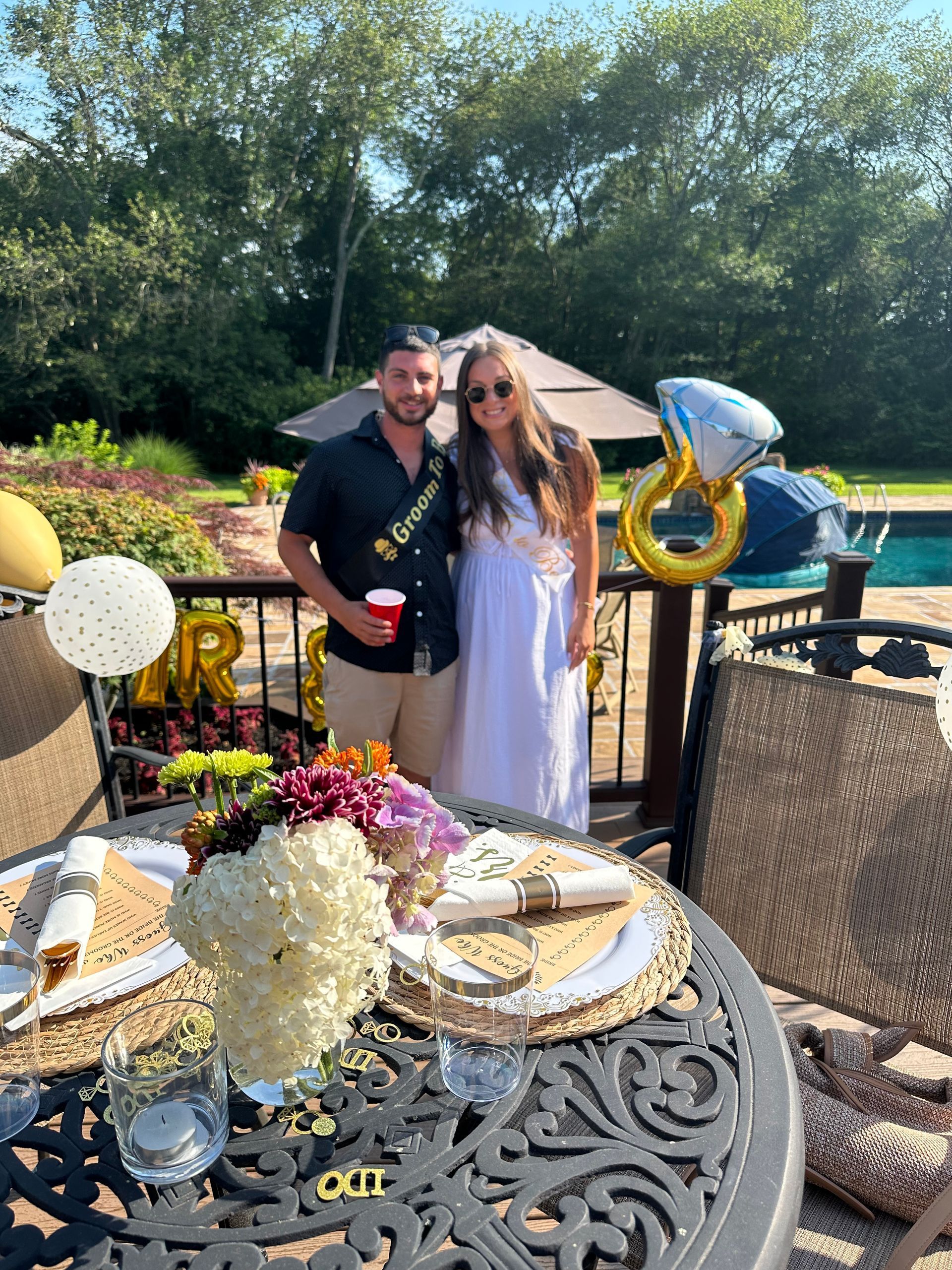 Couple celebrates engagement outdoors by decorated table and pool.