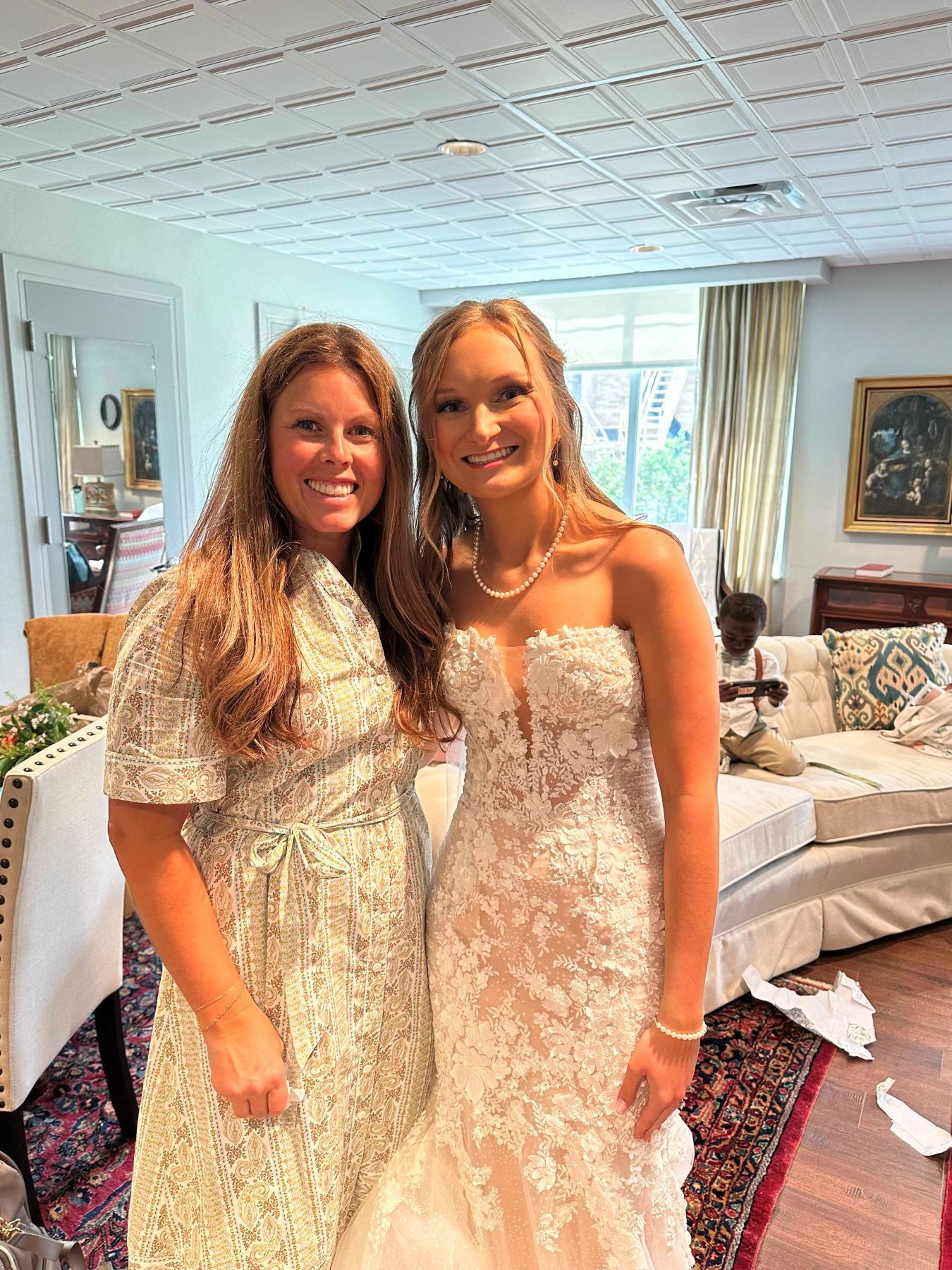 Woman in white dress and woman in patterned dress smiling indoors.