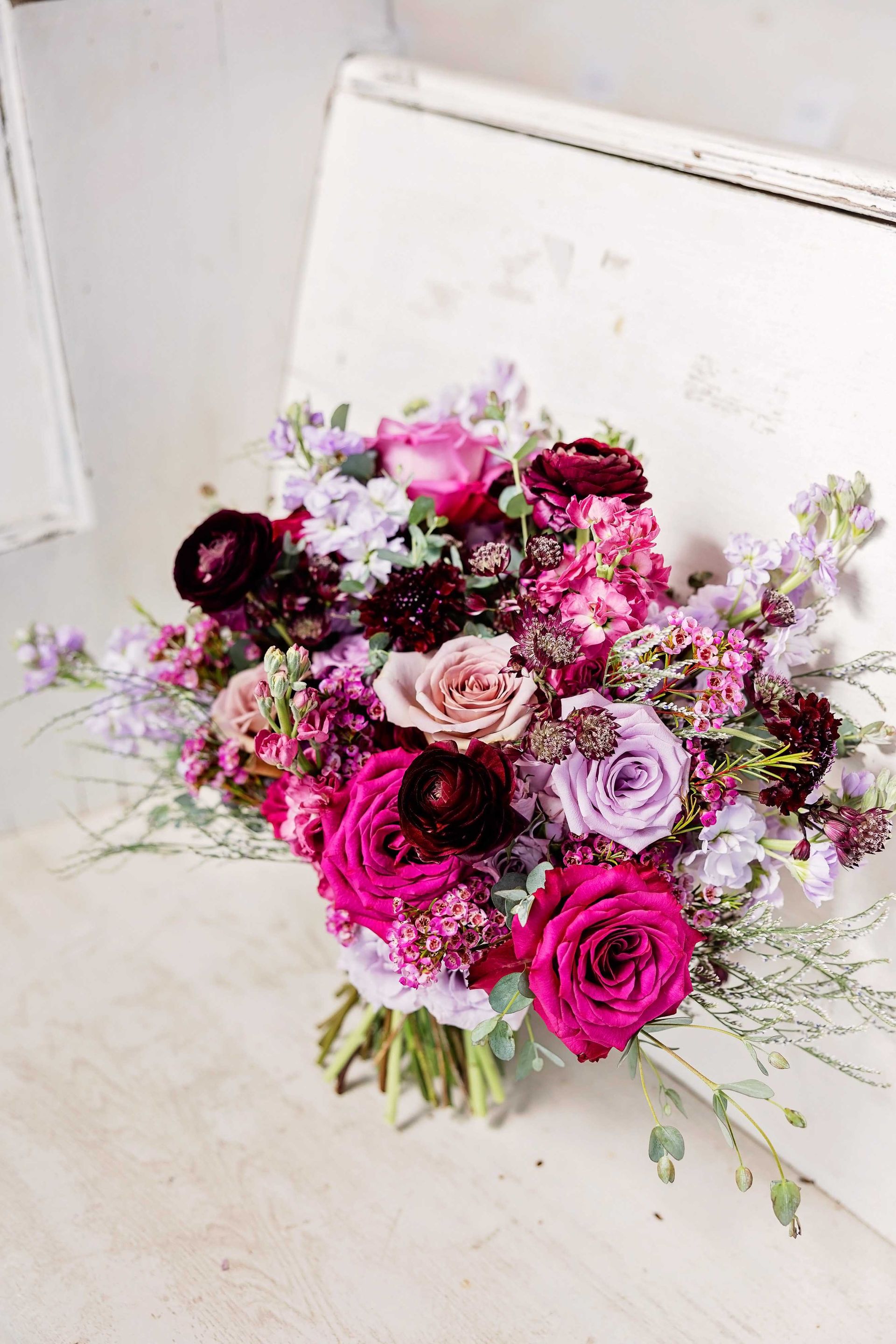 Bouquet of vibrant pink and purple flowers with greenery, resting on a distressed white surface.