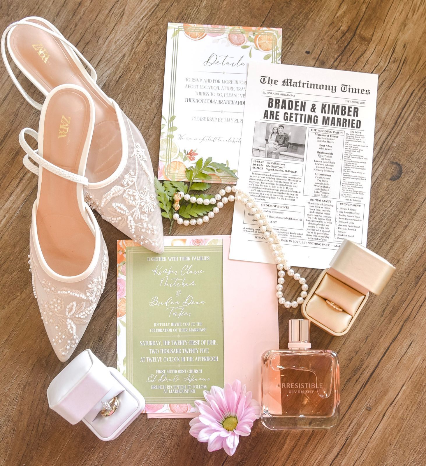 Wedding flat lay: shoes, invitations, jewelry, perfume, and rings arranged on a wooden surface in a pastel color scheme.