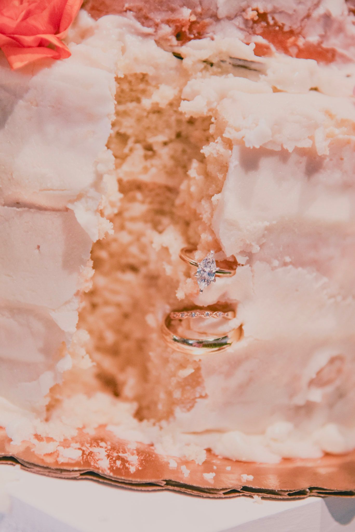 Wedding rings embedded in a partially eaten cake, showing a diamond engagement ring above a gold band.