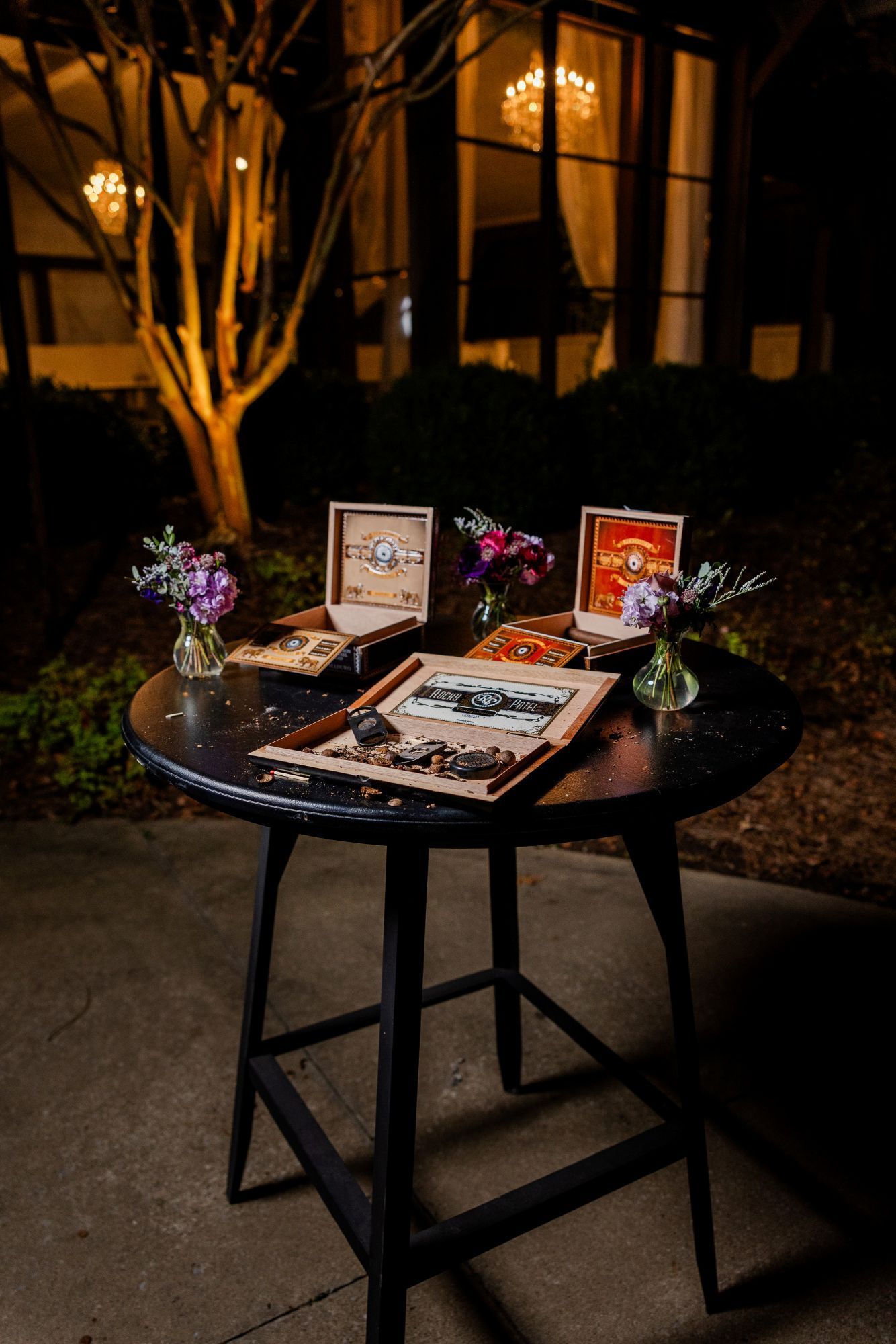 A black table displays open boxes with photos and flowers. The setting is outside at night, in front of a building.