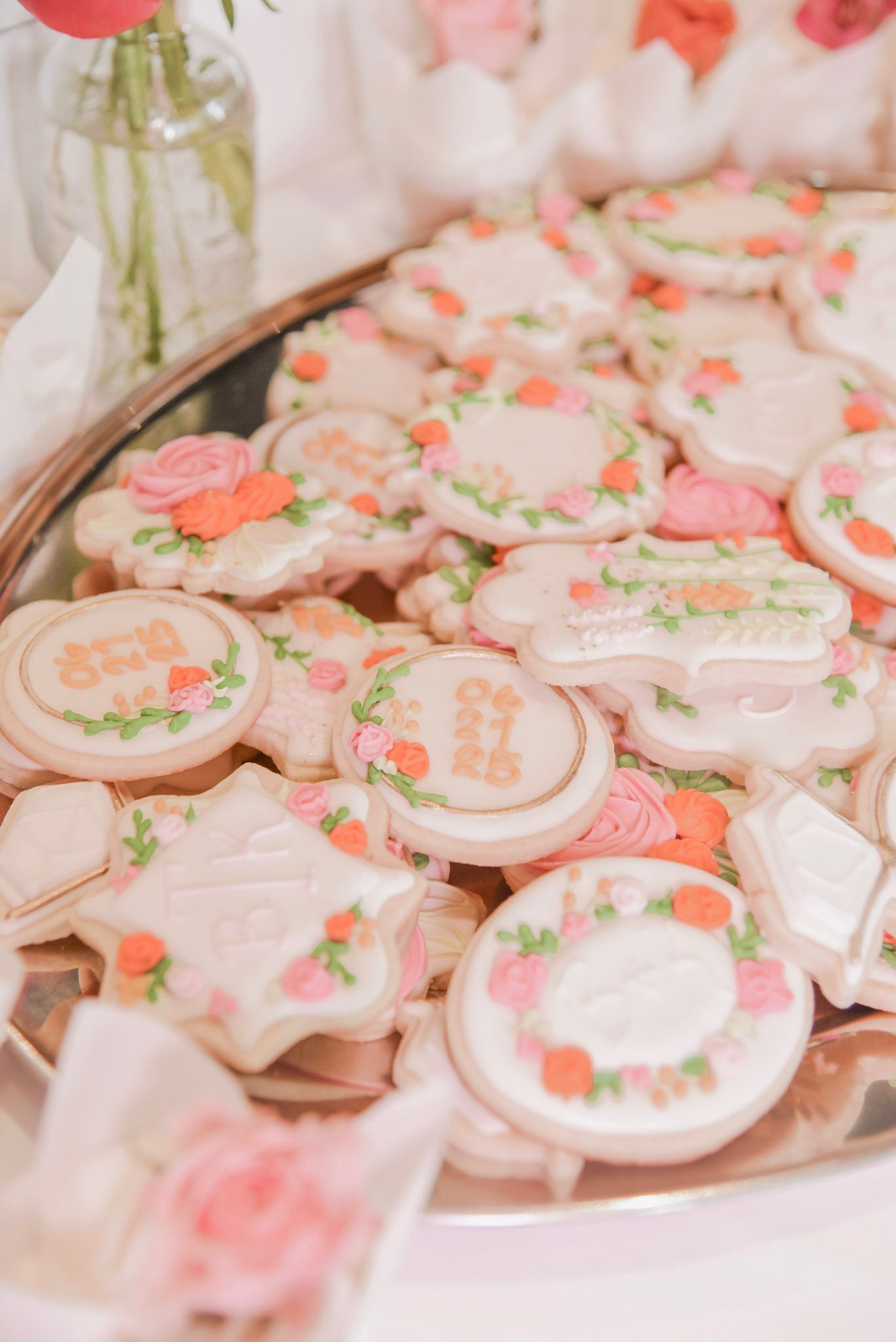 Tray of decorated sugar cookies with floral designs and text in shades of pink, green, and orange.