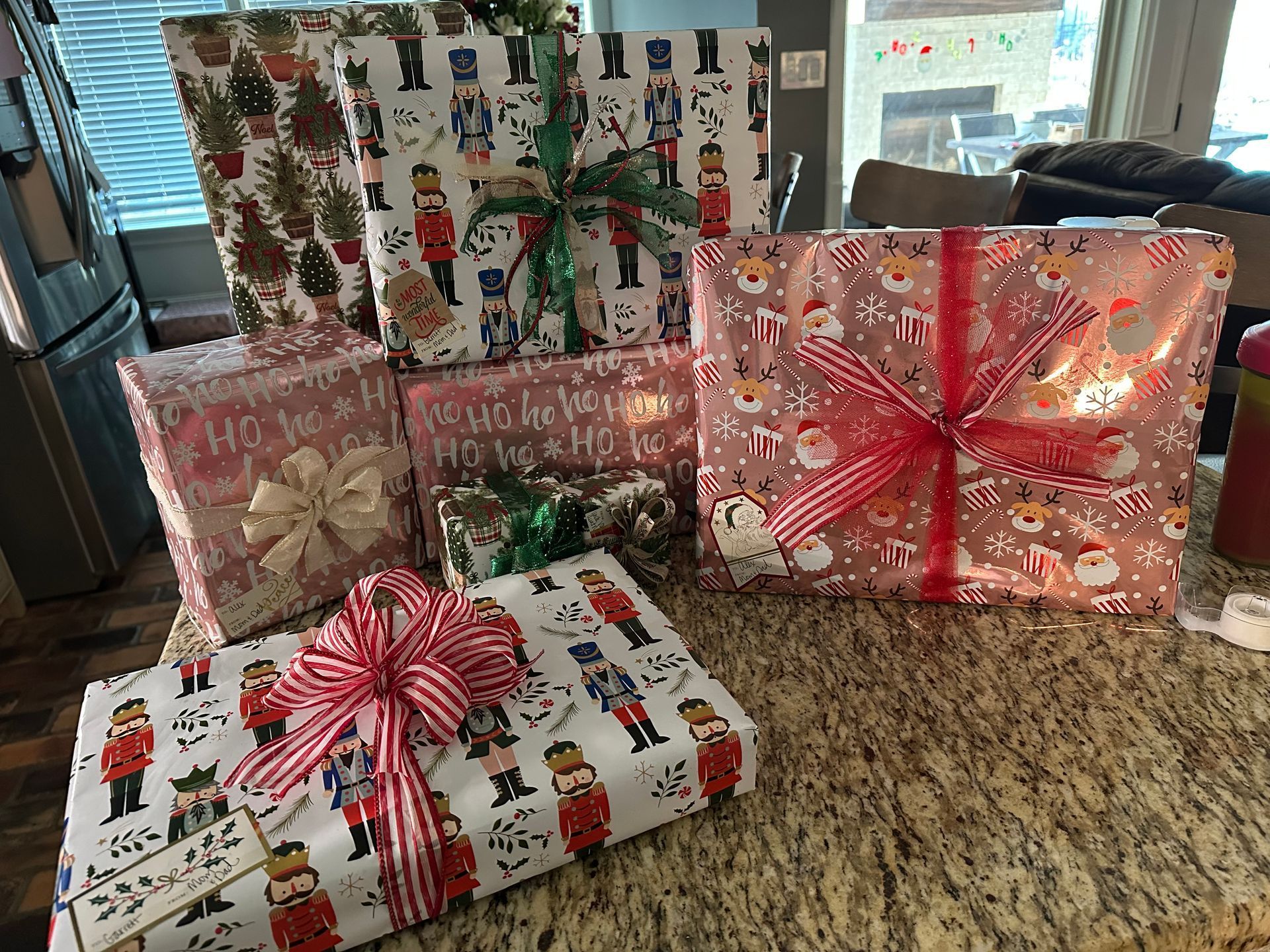 Several Christmas presents wrapped in festive paper with red-and-white striped bows sit on a granite countertop.