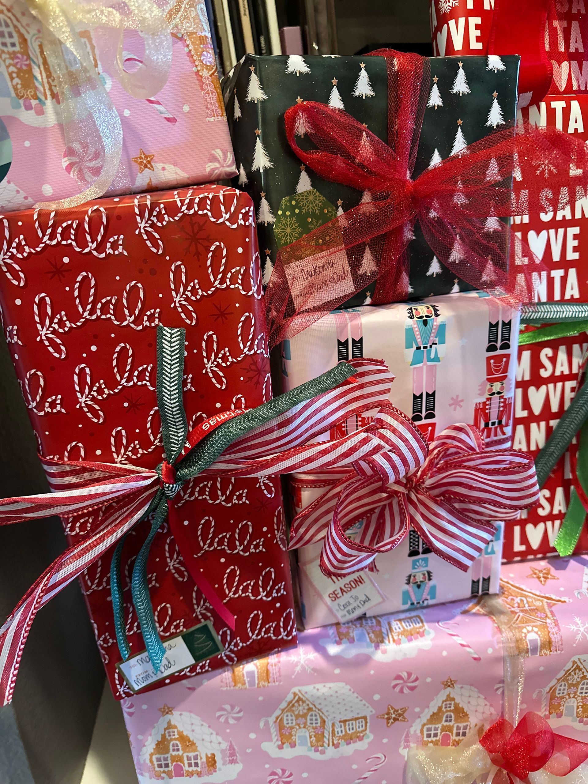 A collection of holiday-wrapped gifts in red, pink, and black with festive patterns, decorated with colorful bows.