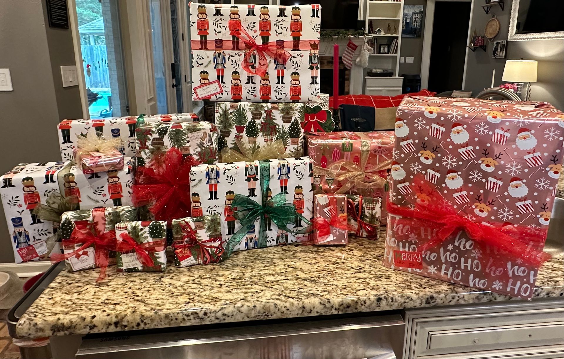 A collection of wrapped Christmas gifts of various sizes sitting on a white cabinet shelf, decorated with festive bows.