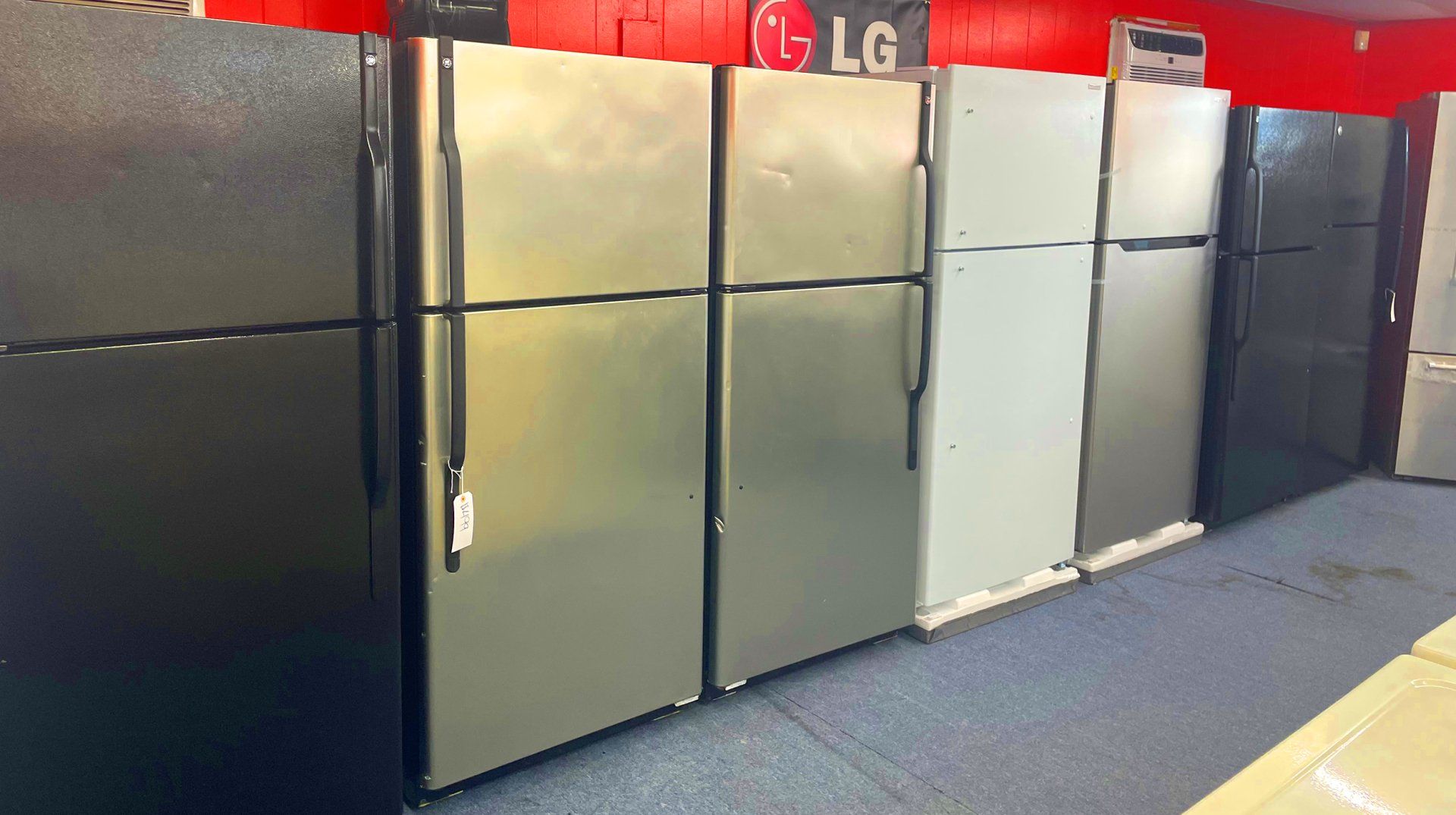 Refrigerators in various colors lined up against a wall in a store.