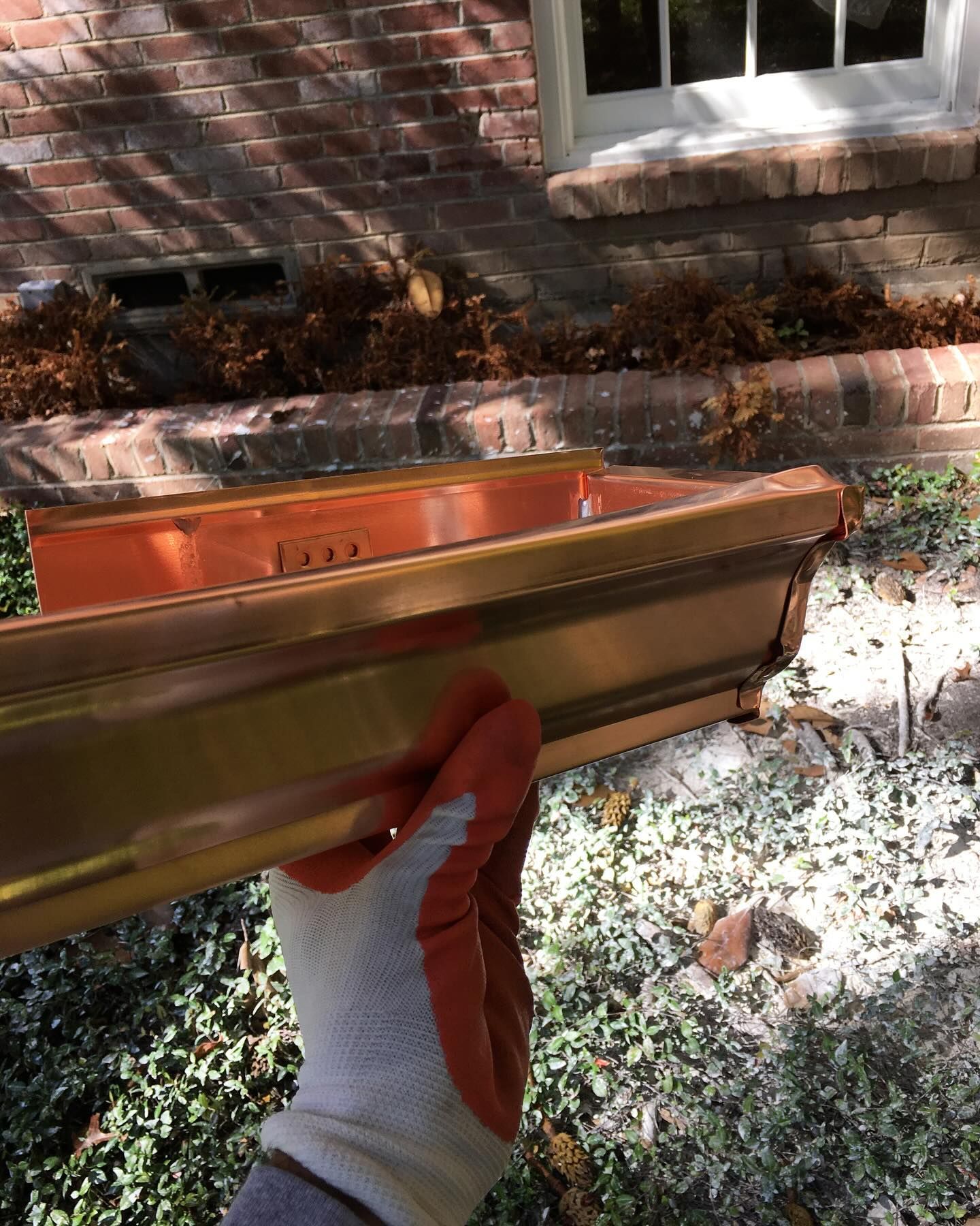 A person wearing red gloves is holding a copper gutter.