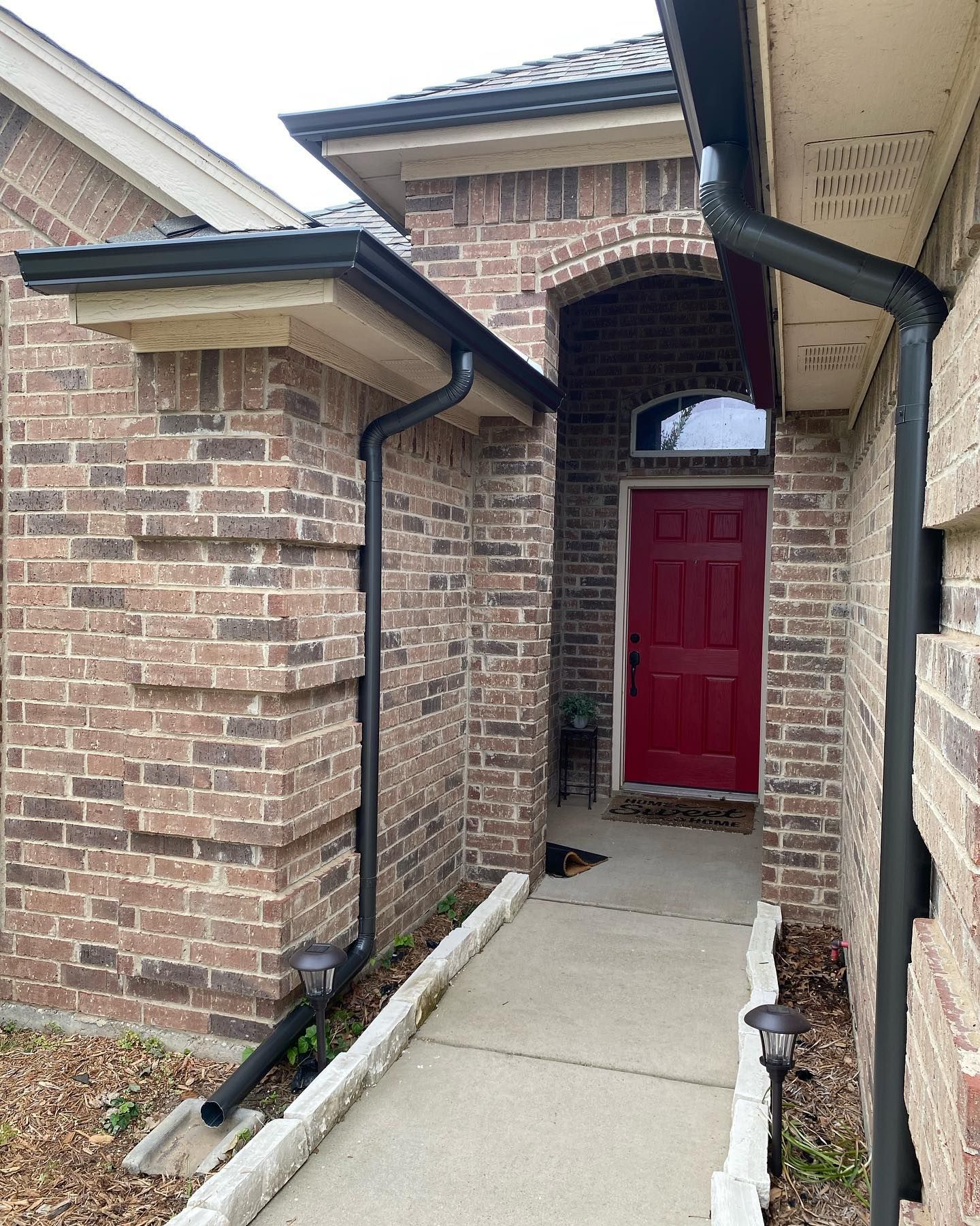 A brick house with a red door and black gutters