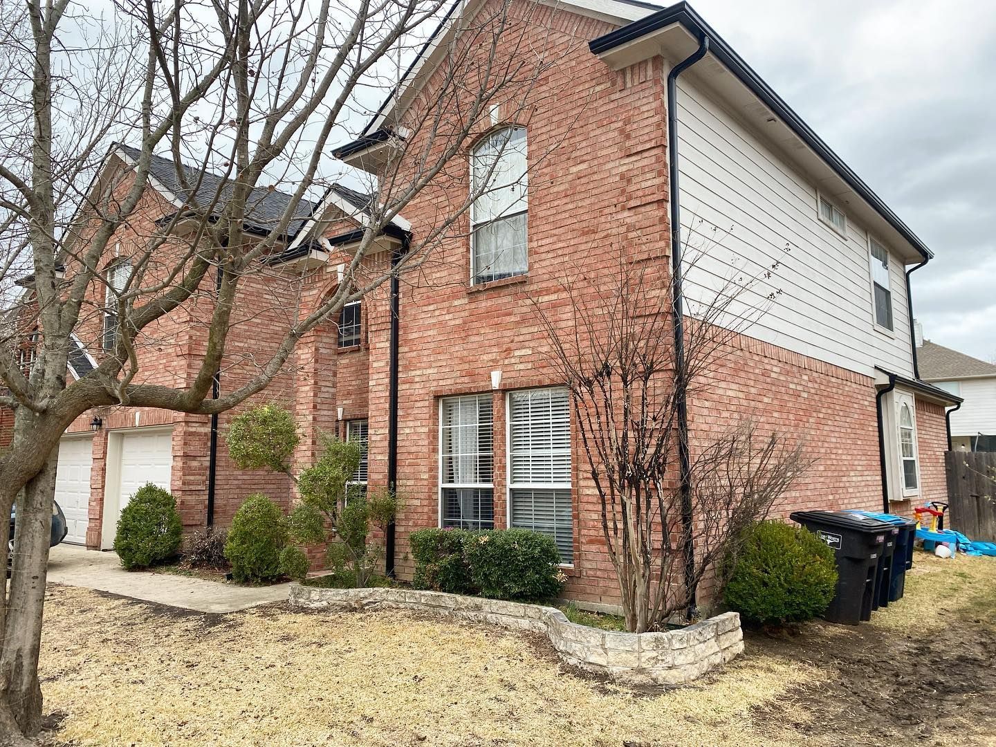 A large brick house with a white siding and a tree in front of it.