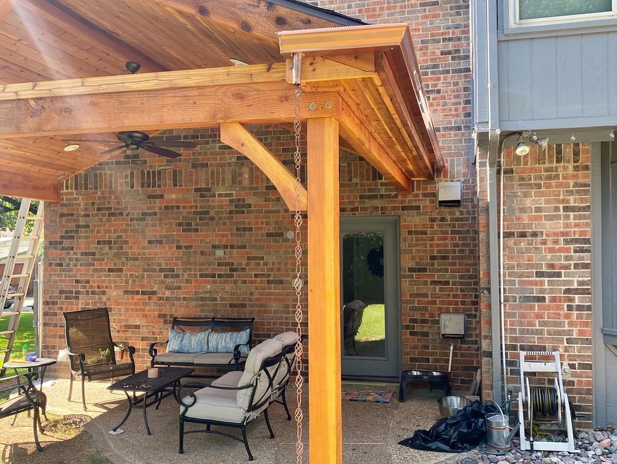 A wooden pergola is sitting in front of a brick house.