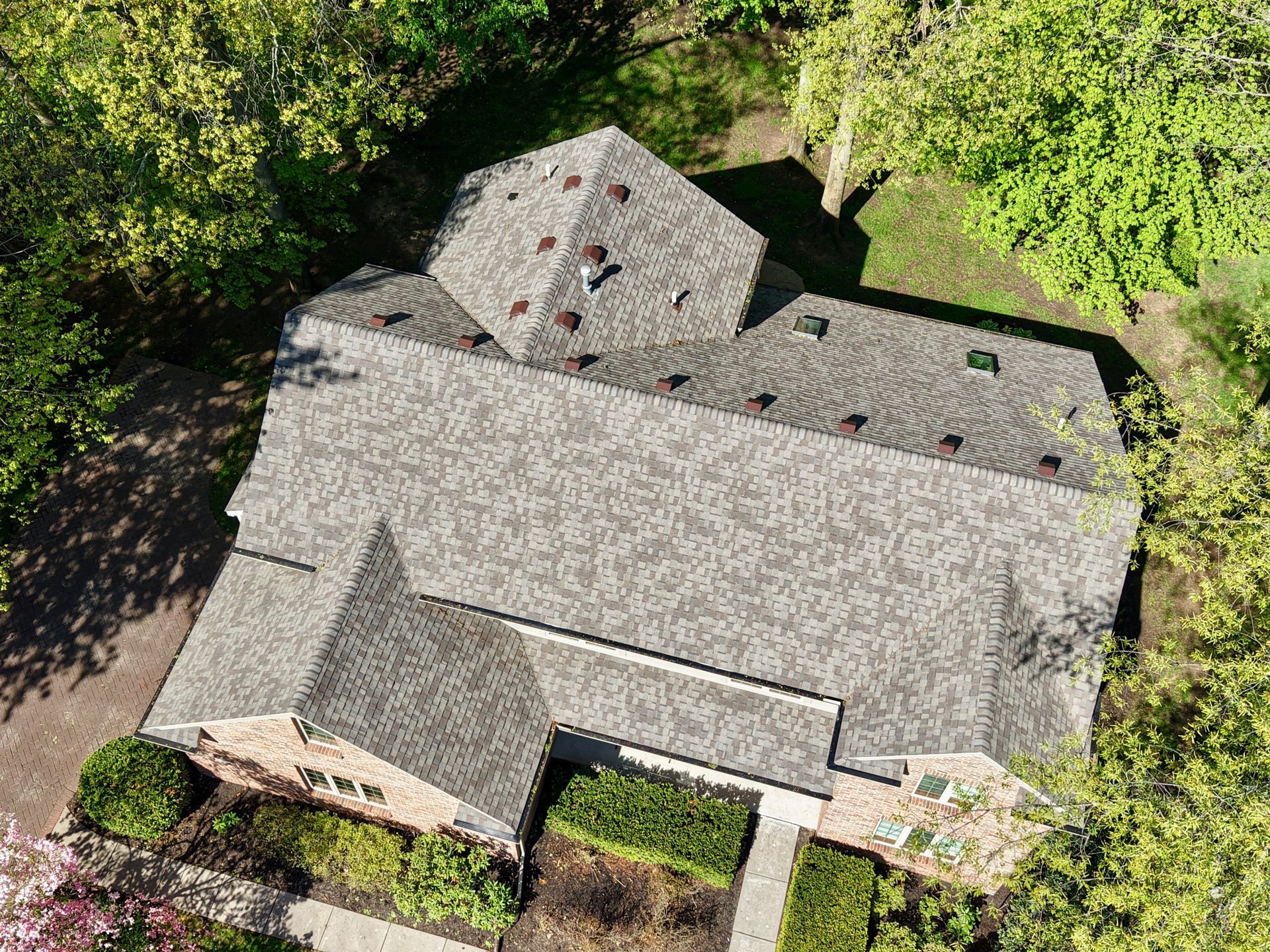 Aerial view of a house with a gray shingled roof surrounded by trees and greenery