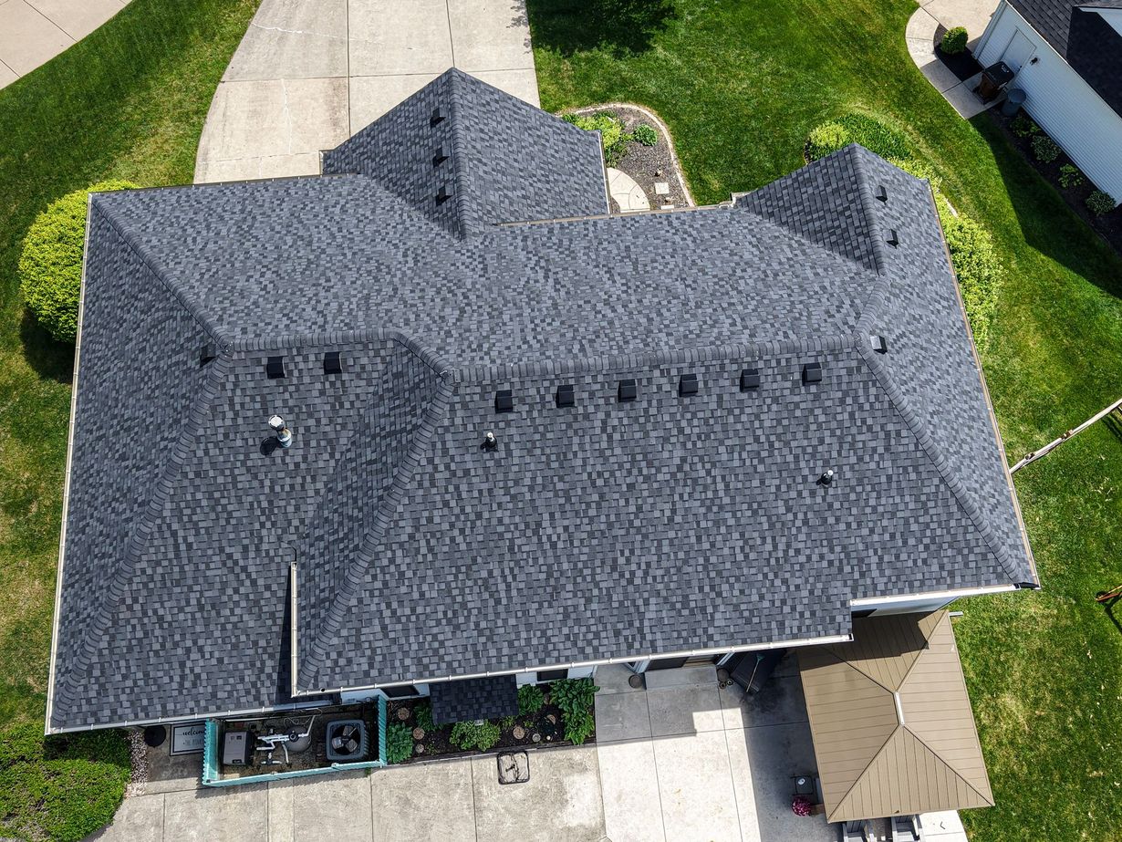 Aerial view of a large gray-shingled house with multiple roof peaks and a green lawn.