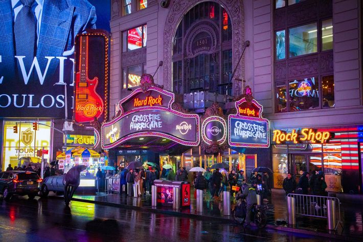 Neon-lit theater and shopfronts on a rainy city street at night, with colorful reflections on wet pavement