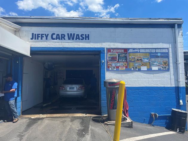 Jiffy Car Wash exterior with a car inside.  A worker stands near the entrance. Blue and white building.