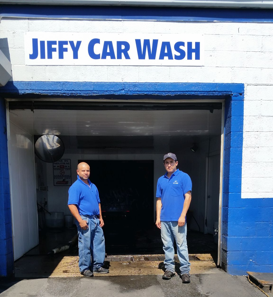 Two men in blue shirts and jeans stand at the entrance of a
