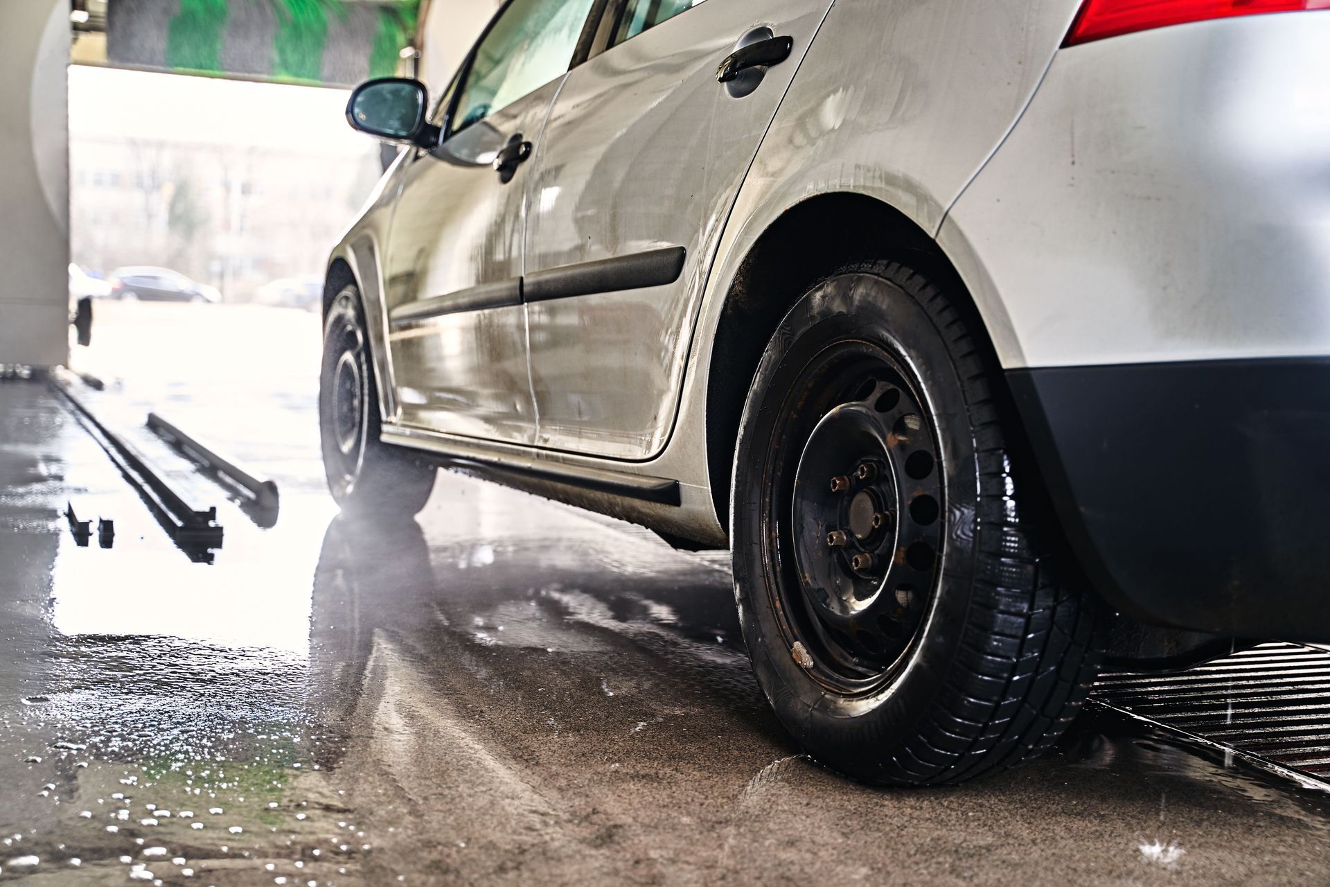 Silver car being washed at a car wash. Water spraying around the tires and undercarriage.
