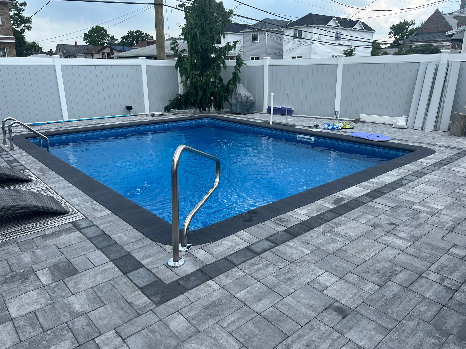White curved lounge chairs in a shallow swimming pool beside a modern patio and blue water
