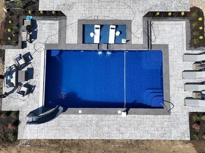 Aerial view of a backyard with a blue rectangular swimming pool, lounge chairs, and stone patio.