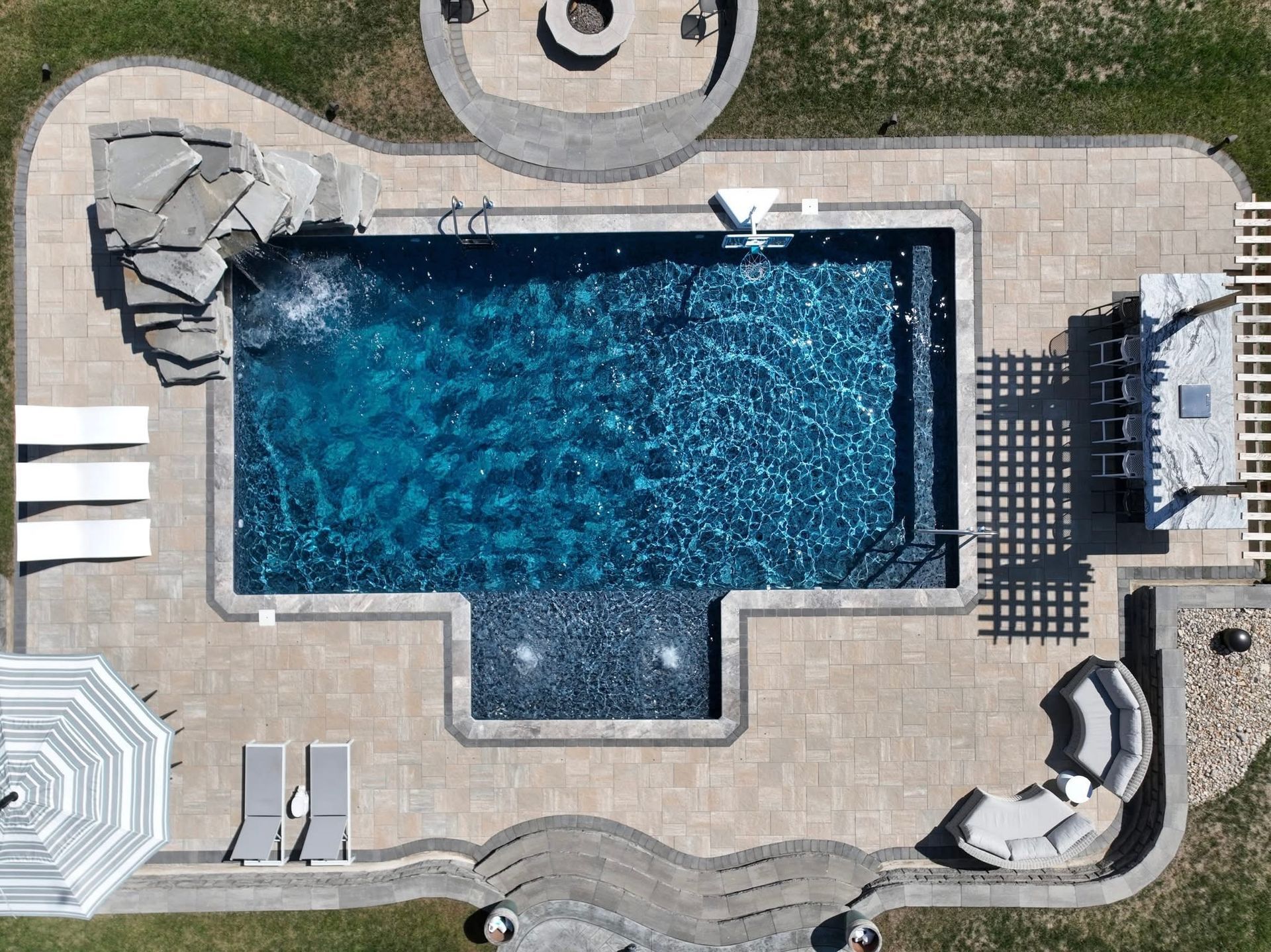 Overhead view of a backyard pool with lounge chairs, deck chairs, and a hot tub