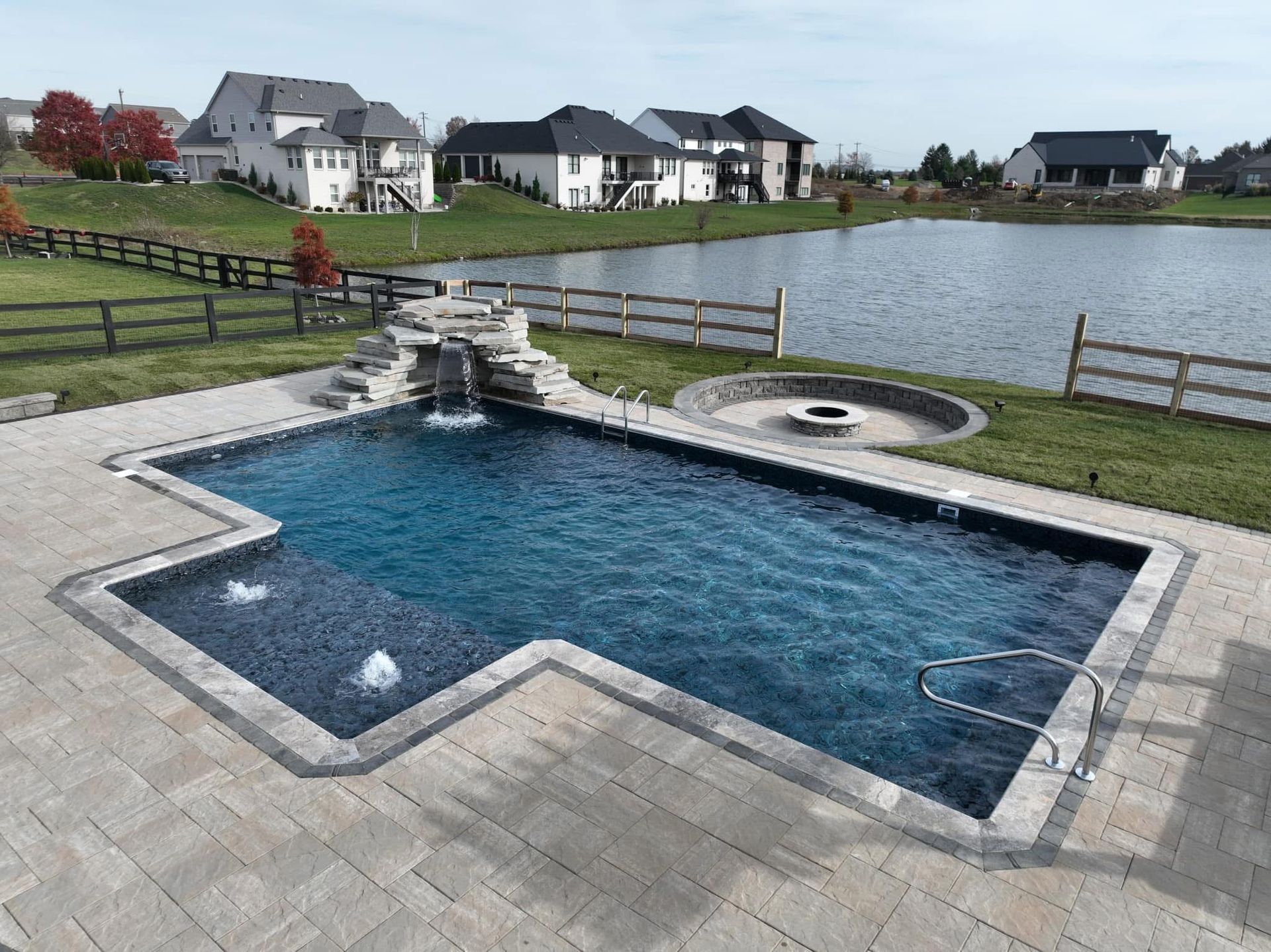 Backyard swimming pool with stone patio, waterfall, and a pond in the background