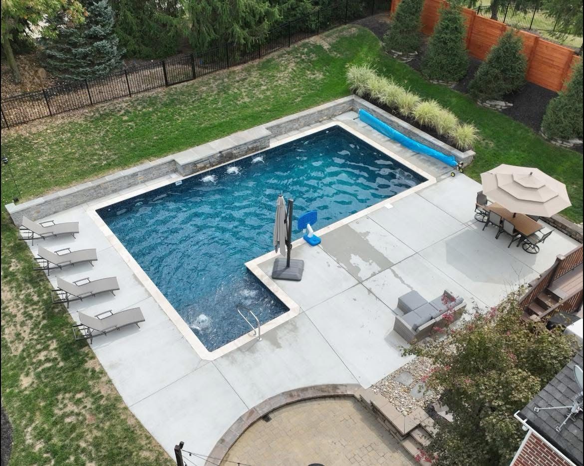 Backyard pool with blue water, patio chairs, umbrella, and surrounding greenery