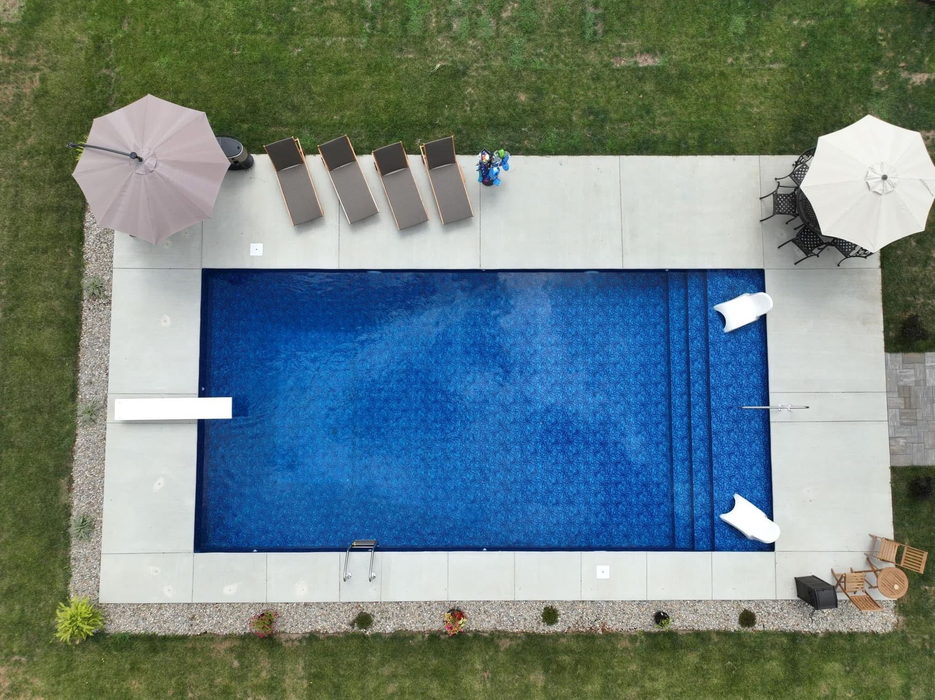 Overhead view of a backyard pool with blue water, lounge chairs, umbrellas, and patio decking