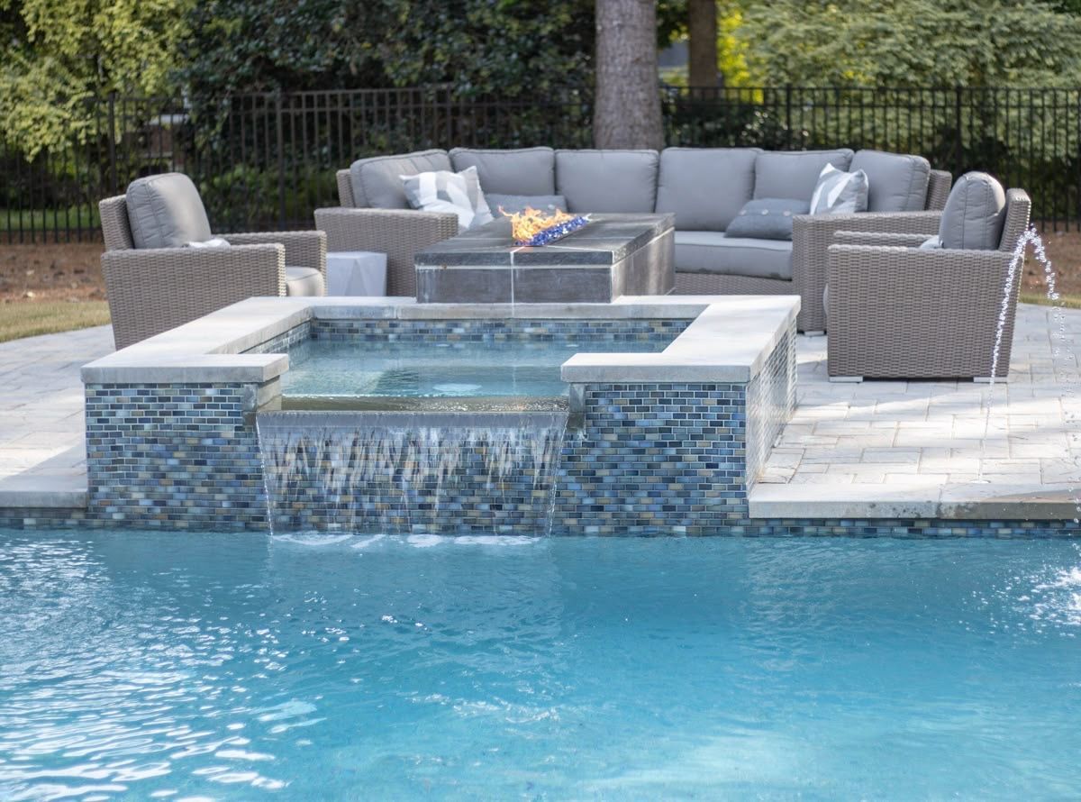 Modern backyard pool with a raised spa, wicker seating, and stone patio seating area