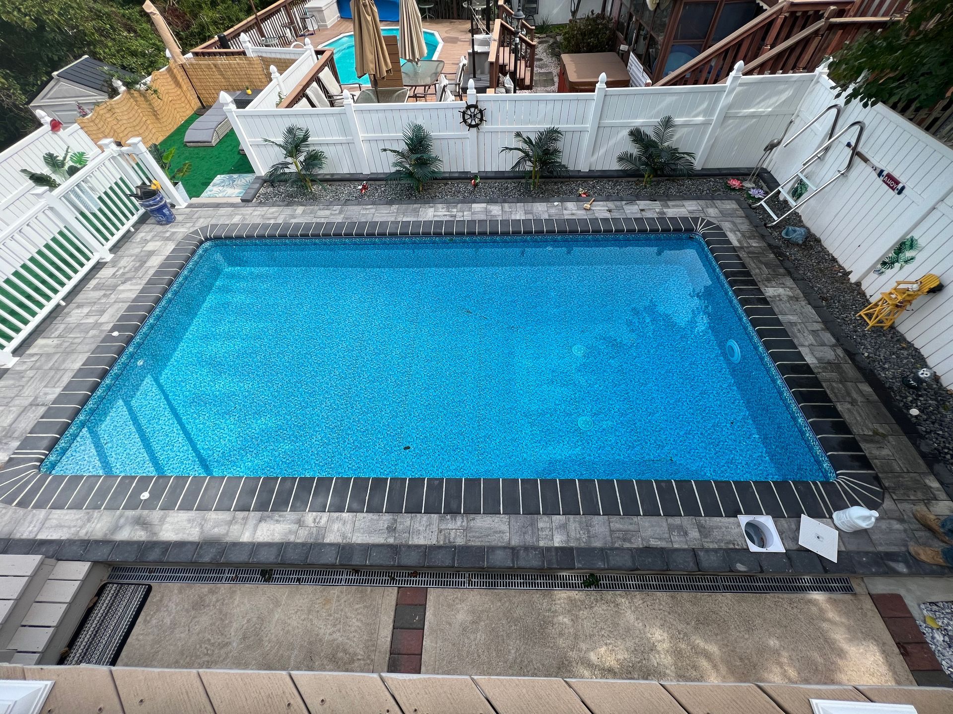 Backyard swimming pool with blue water, white fence, and stone patio surrounds