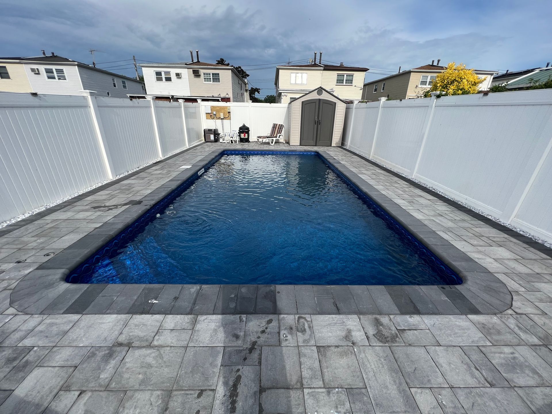 Rectangular backyard swimming pool with blue water, gray stone deck, and white fence on both sides