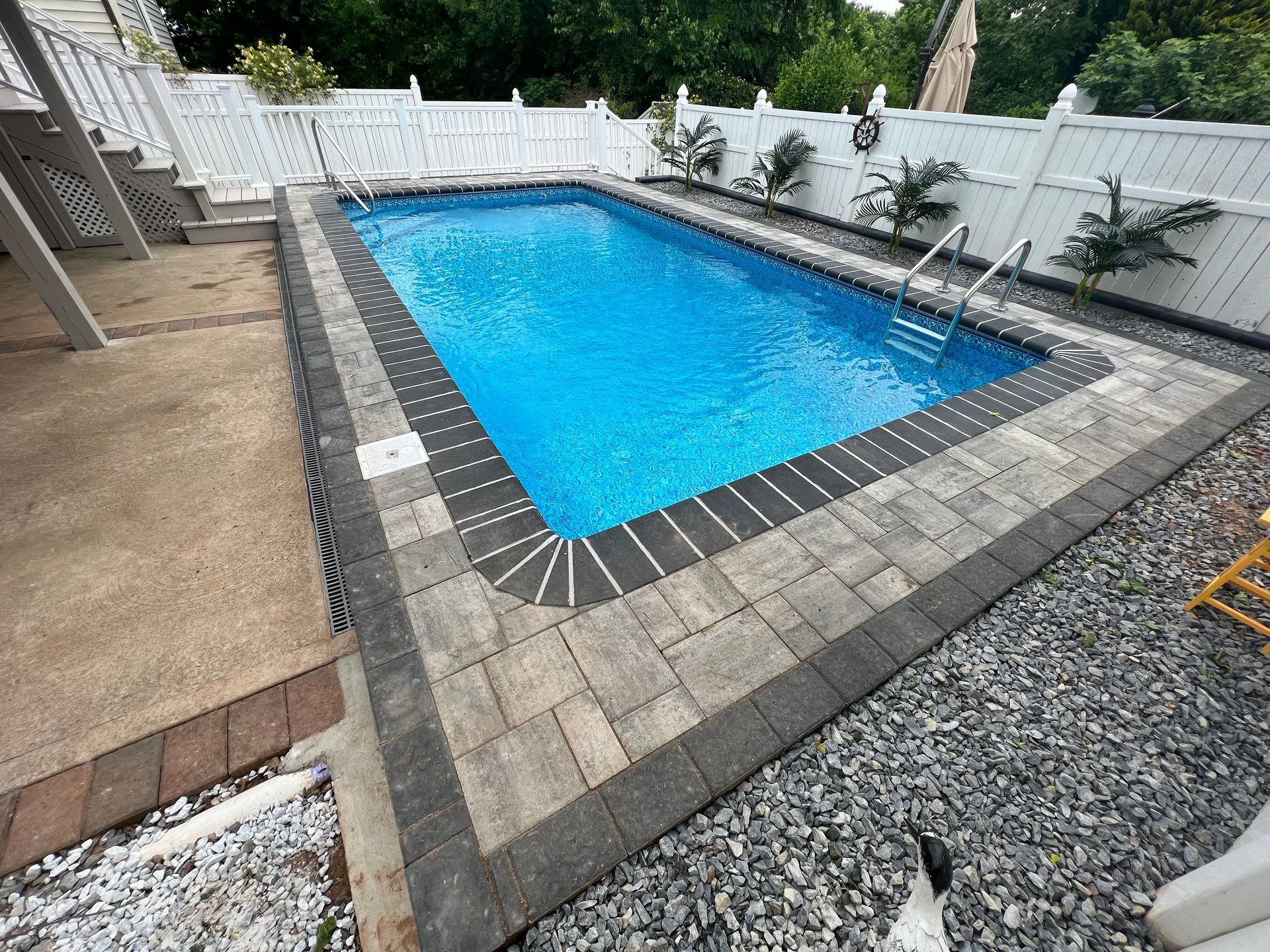 Rectangular backyard pool with blue water, gray pavers, and a white fence surrounding it