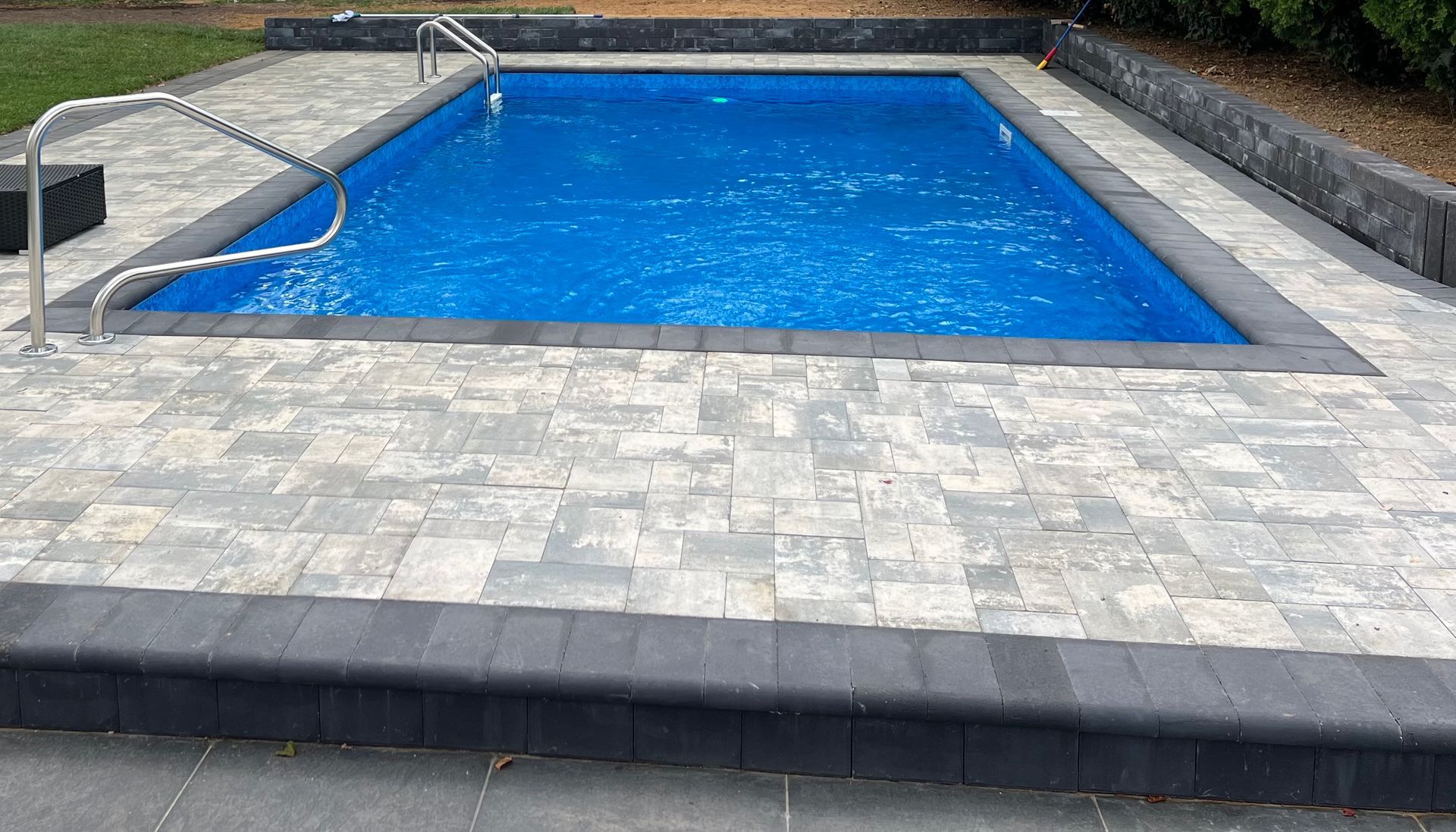 Blue rectangular swimming pool surrounded by light stone paving and steps