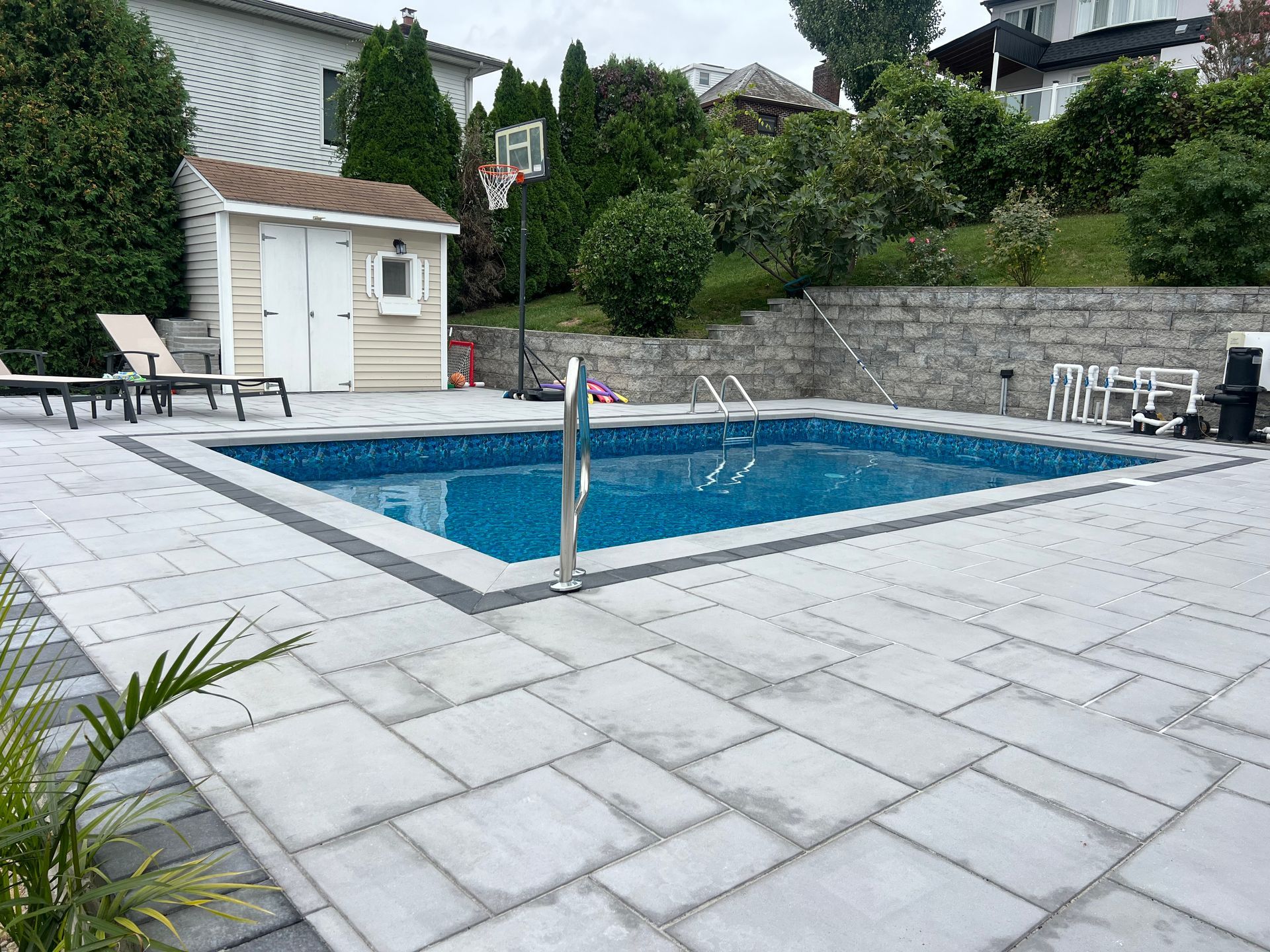 Backyard swimming pool with blue water, stone patio, lounge chairs, and a small shed nearby