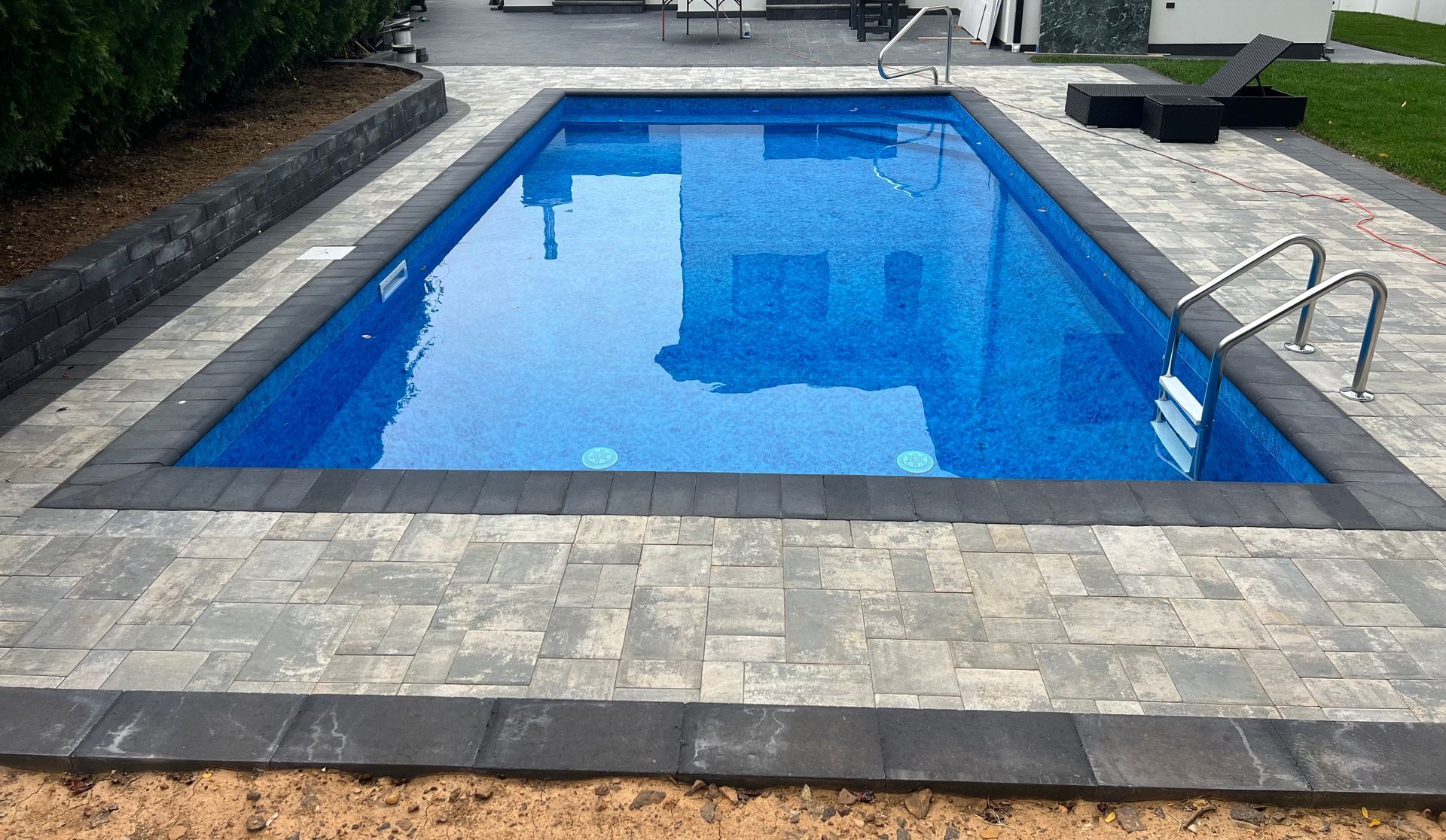 Rectangular blue swimming pool with stone patio and metal ladder at the right side