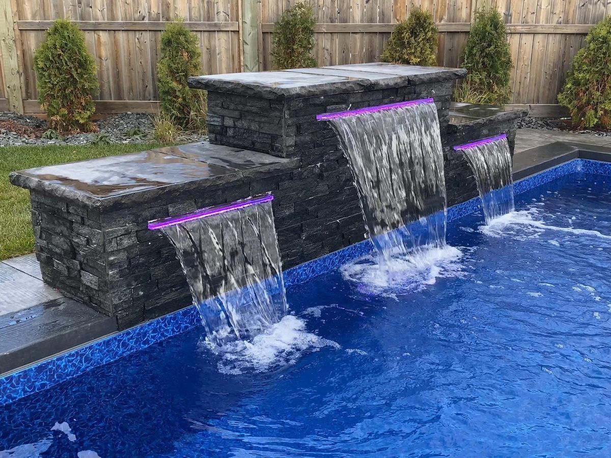 Modern backyard pool with dark stone waterfall features spilling into blue water