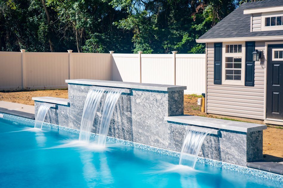 Backyard pool with a stone water feature and cascading waterfalls beside a modern pool house