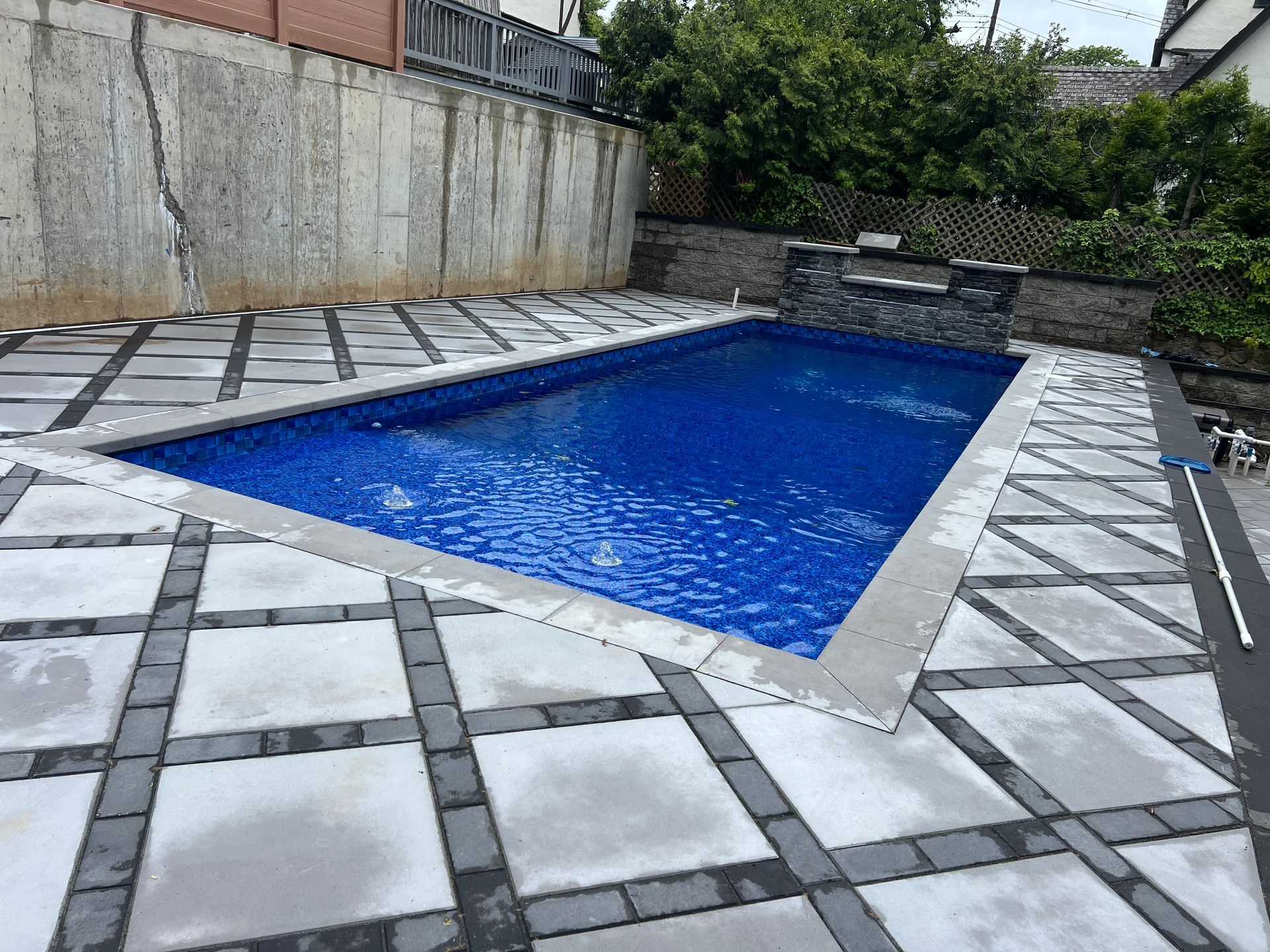 Backyard swimming pool with blue water, surrounded by gray tiled patio and stone walls