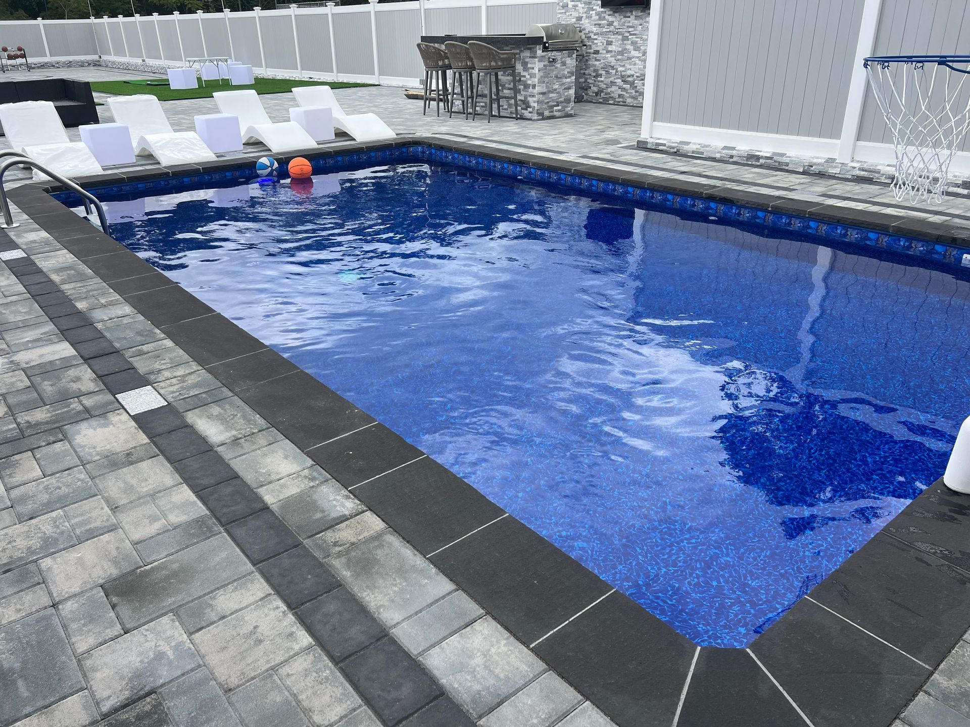 Backyard swimming pool with blue water, white lounge chairs, and a fence surround