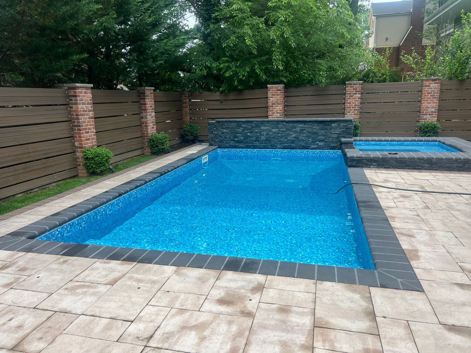 Backyard swimming pool with blue water, brick privacy walls, and stone patio tiles